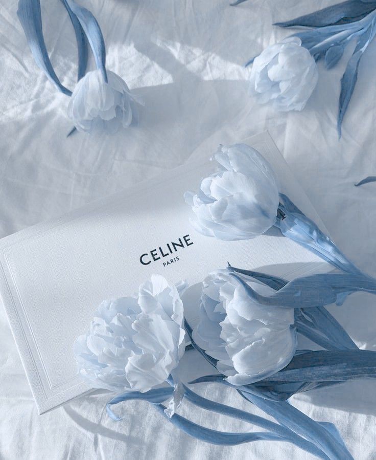 Uma bolsa Celine está cercada por flores azuis em uma cama.