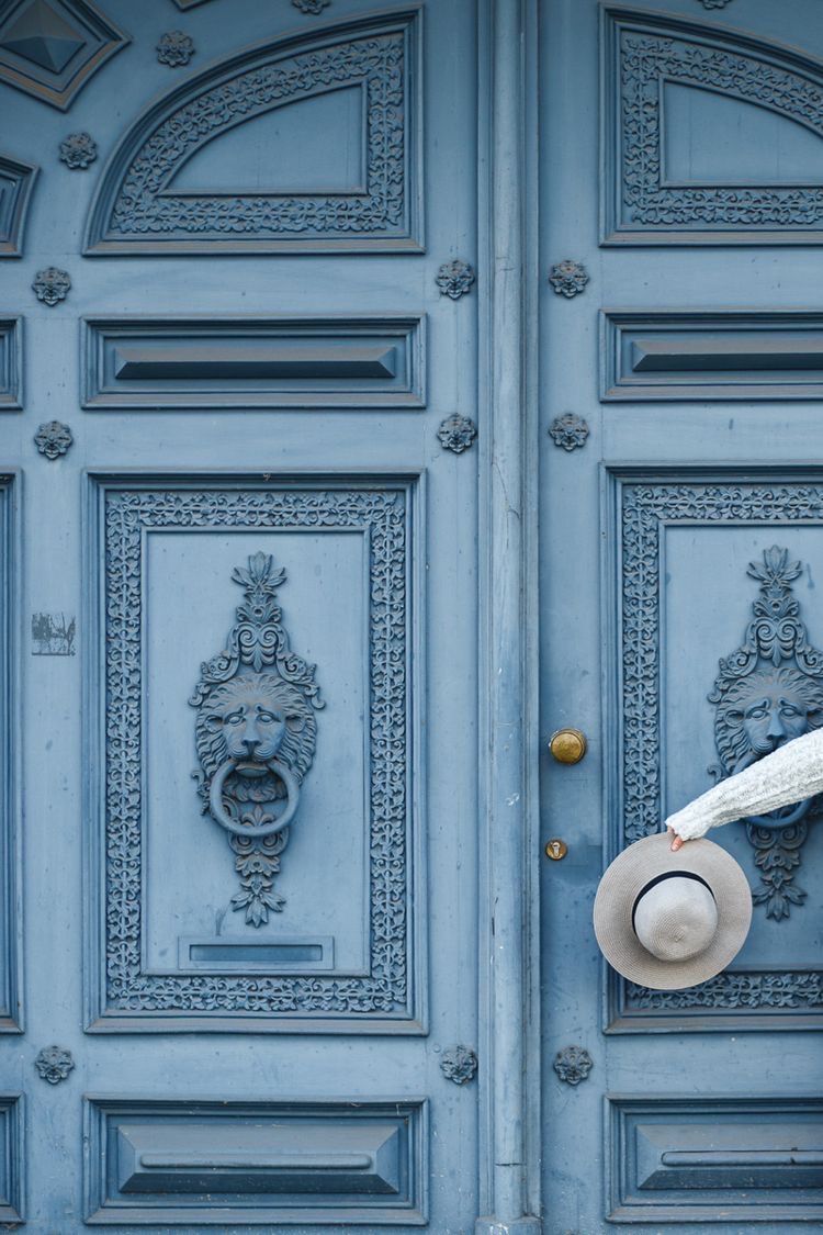 Uma pessoa está segurando um chapéu em frente a uma porta azul.
