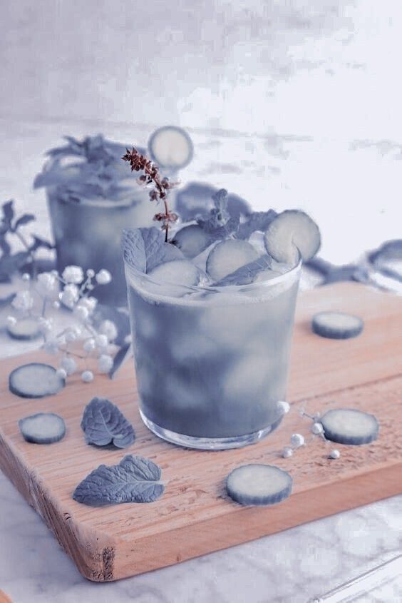 Uma bebida azul em um copo sobre uma tábua de corte de madeira.