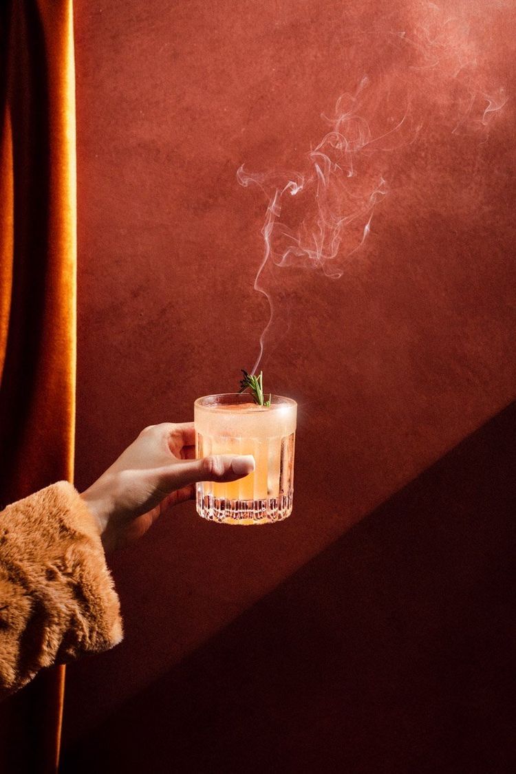 Uma pessoa está segurando um copo de uísque com fumaça saindo dele.