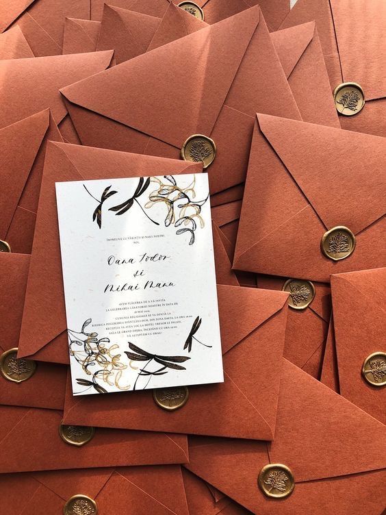 Uma pilha de envelopes marrons com um convite de casamento em cima deles.