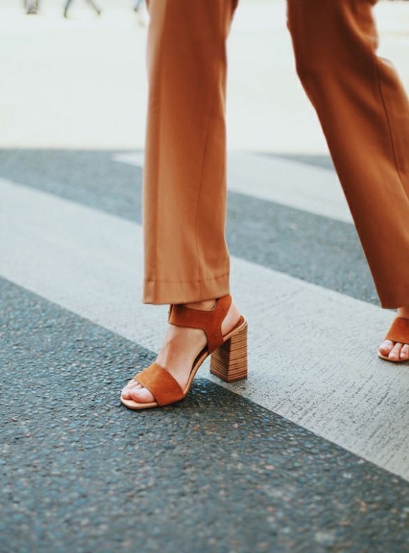 Uma mulher vestindo calças marrons e sandálias marrons está atravessando uma rua.