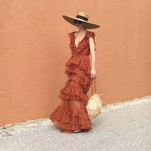 Uma mulher usando um vestido vermelho e um chapéu de palha está parada em frente a uma parede.