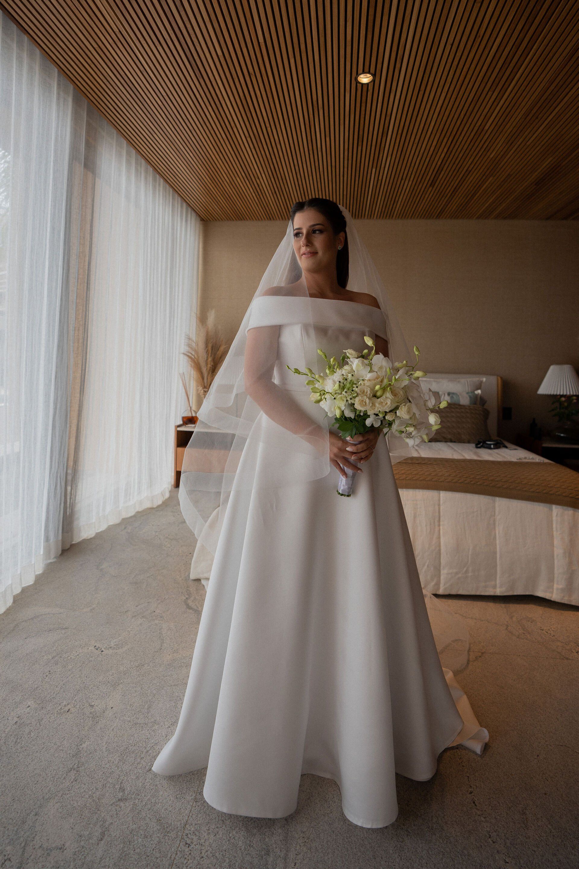 A noiva está usando um vestido de noiva branco e segurando um buquê de flores.