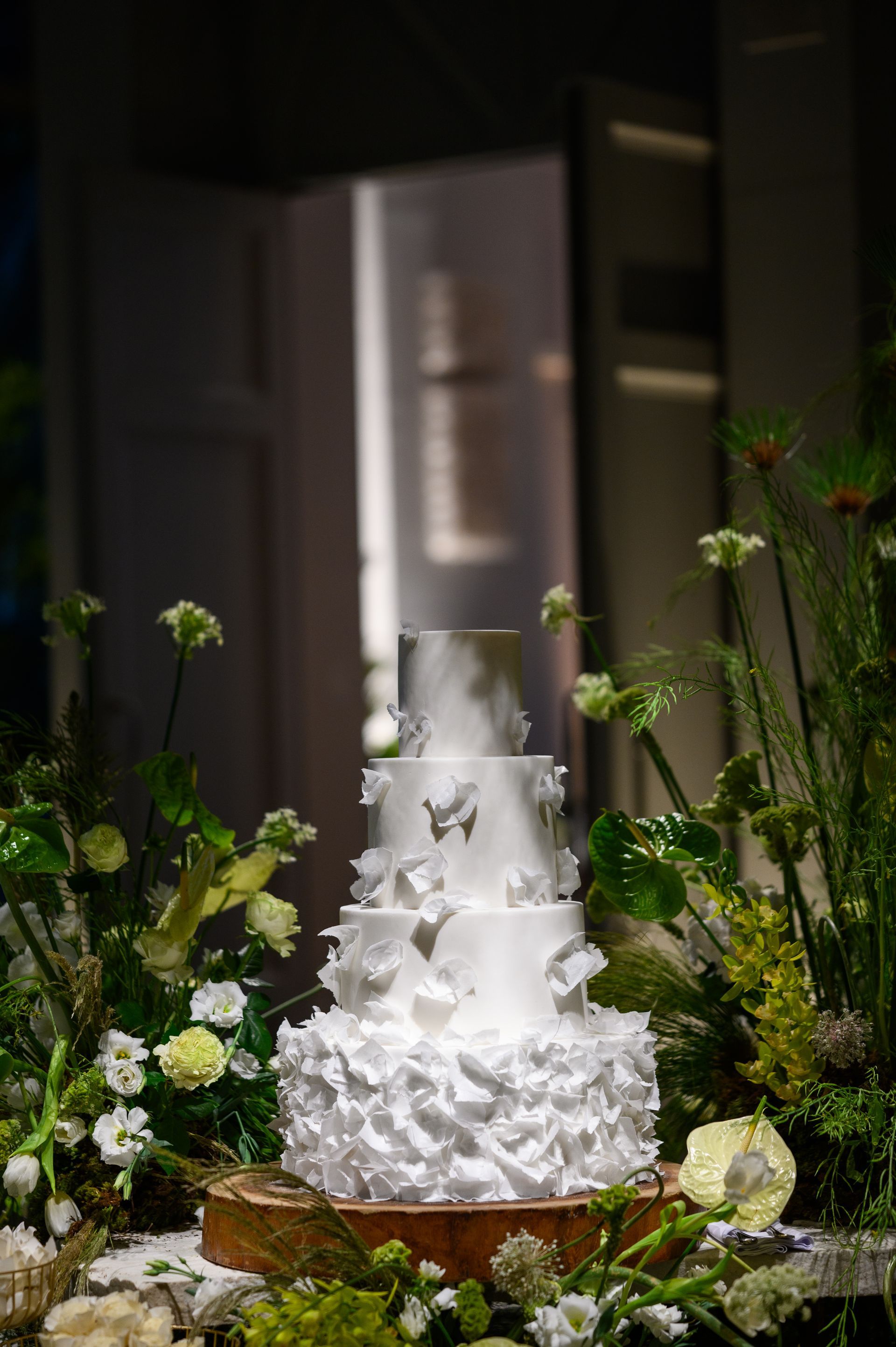 Um bolo de casamento branco está sobre uma mesa de madeira cercado por flores.