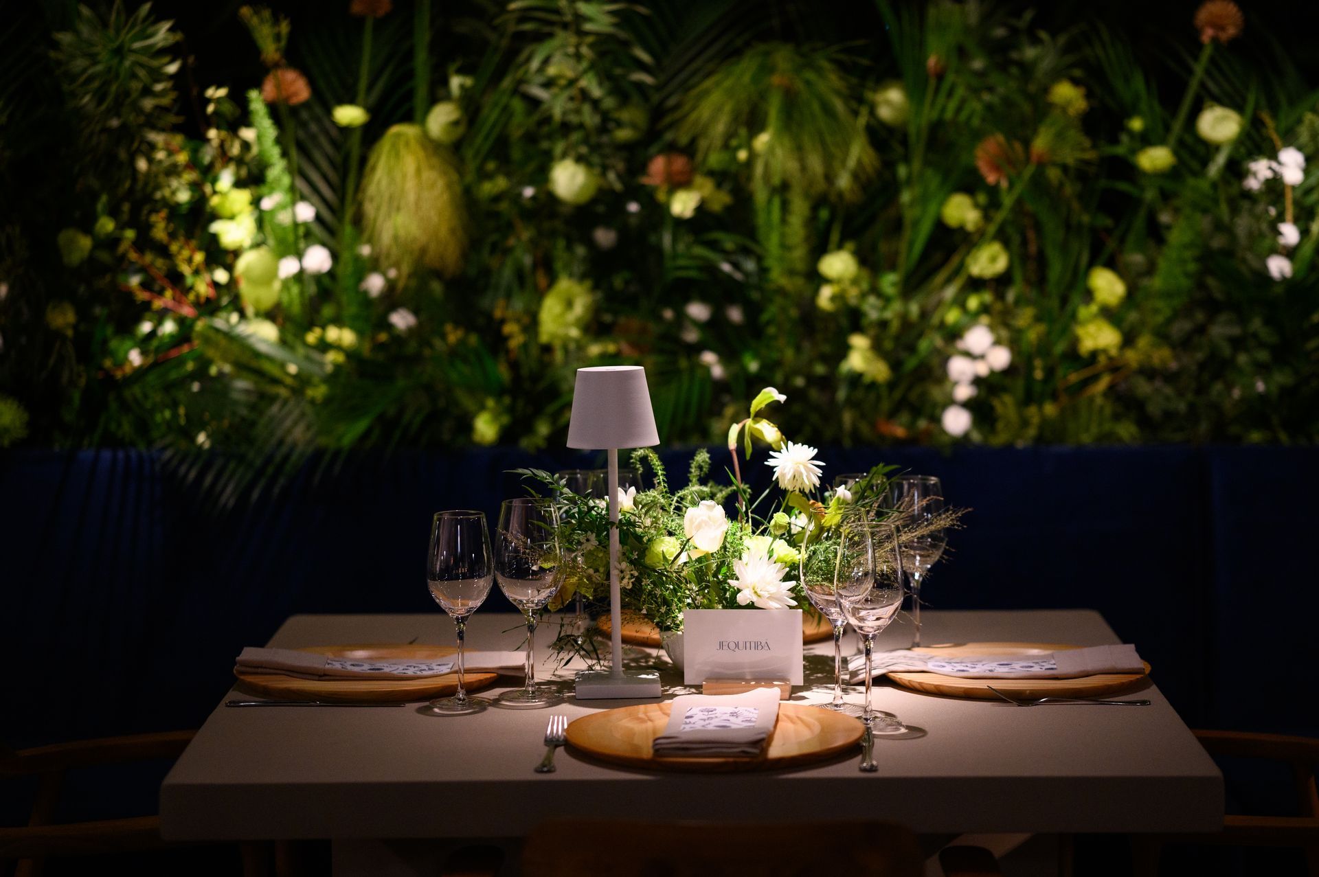 Uma mesa posta para um jantar em frente a uma parede de flores.
