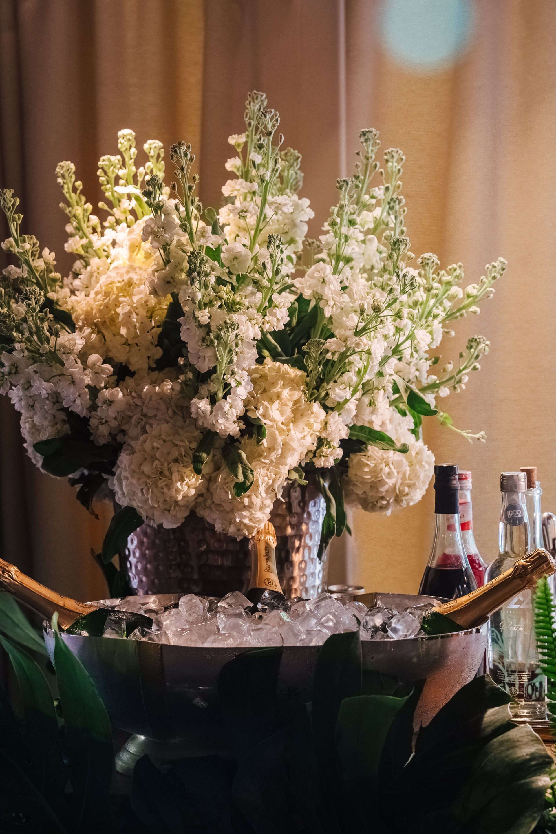 Um vaso cheio de flores brancas está sobre uma mesa ao lado de um balde de gelo.