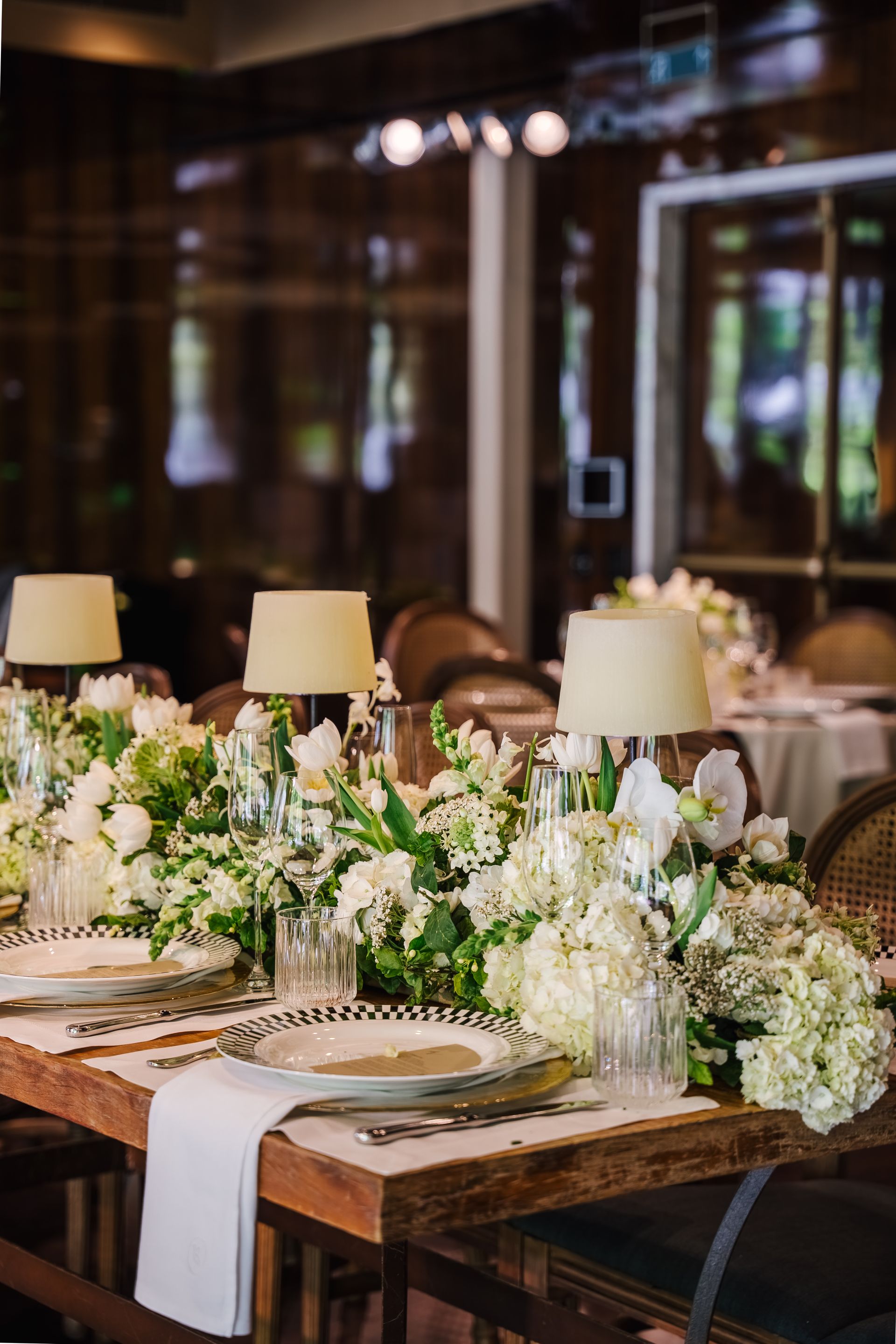 Uma longa mesa com pratos, copos, velas e flores.