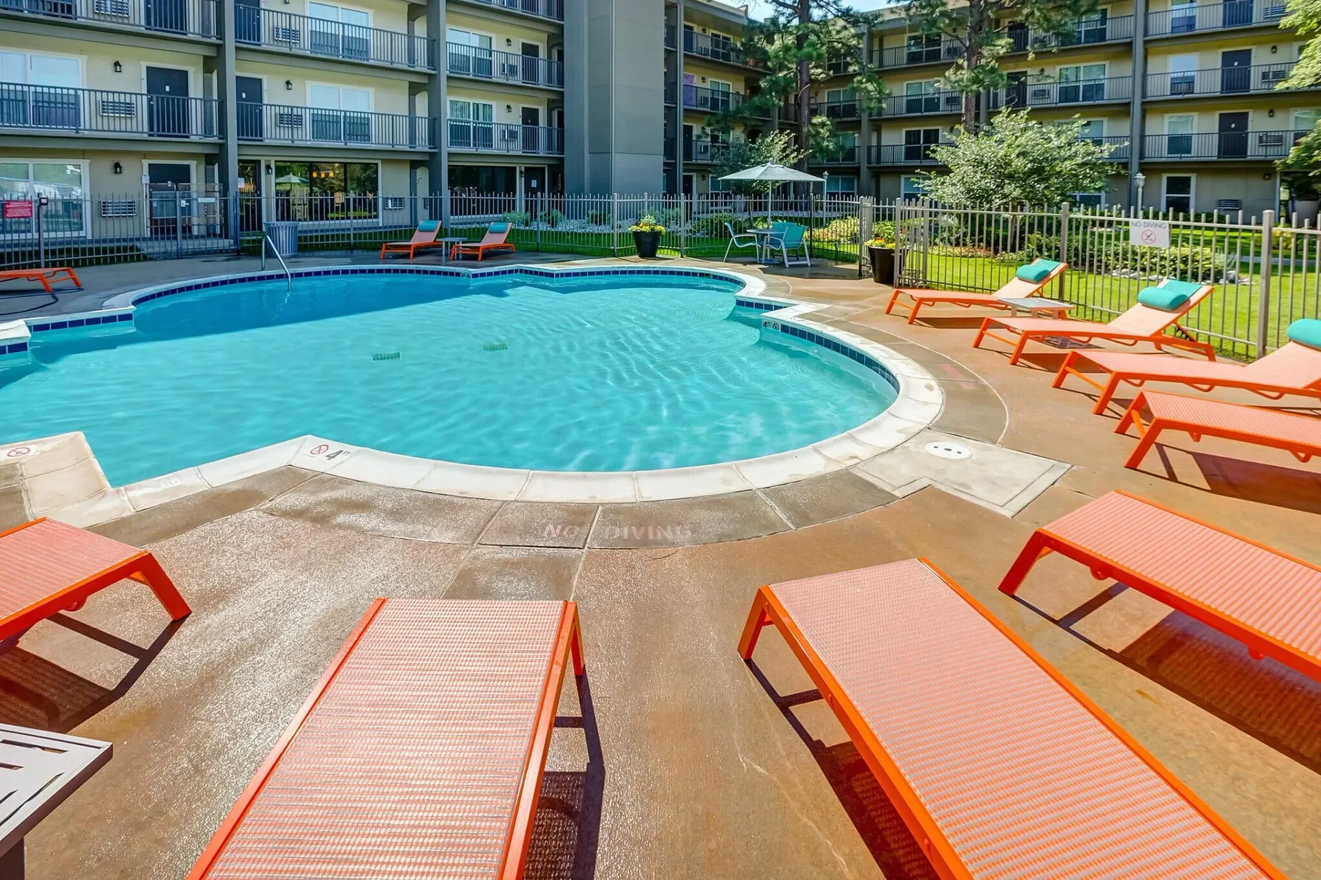 Resort pool with orange lounge chairs and apartment balconies around a turquoise swimming pool