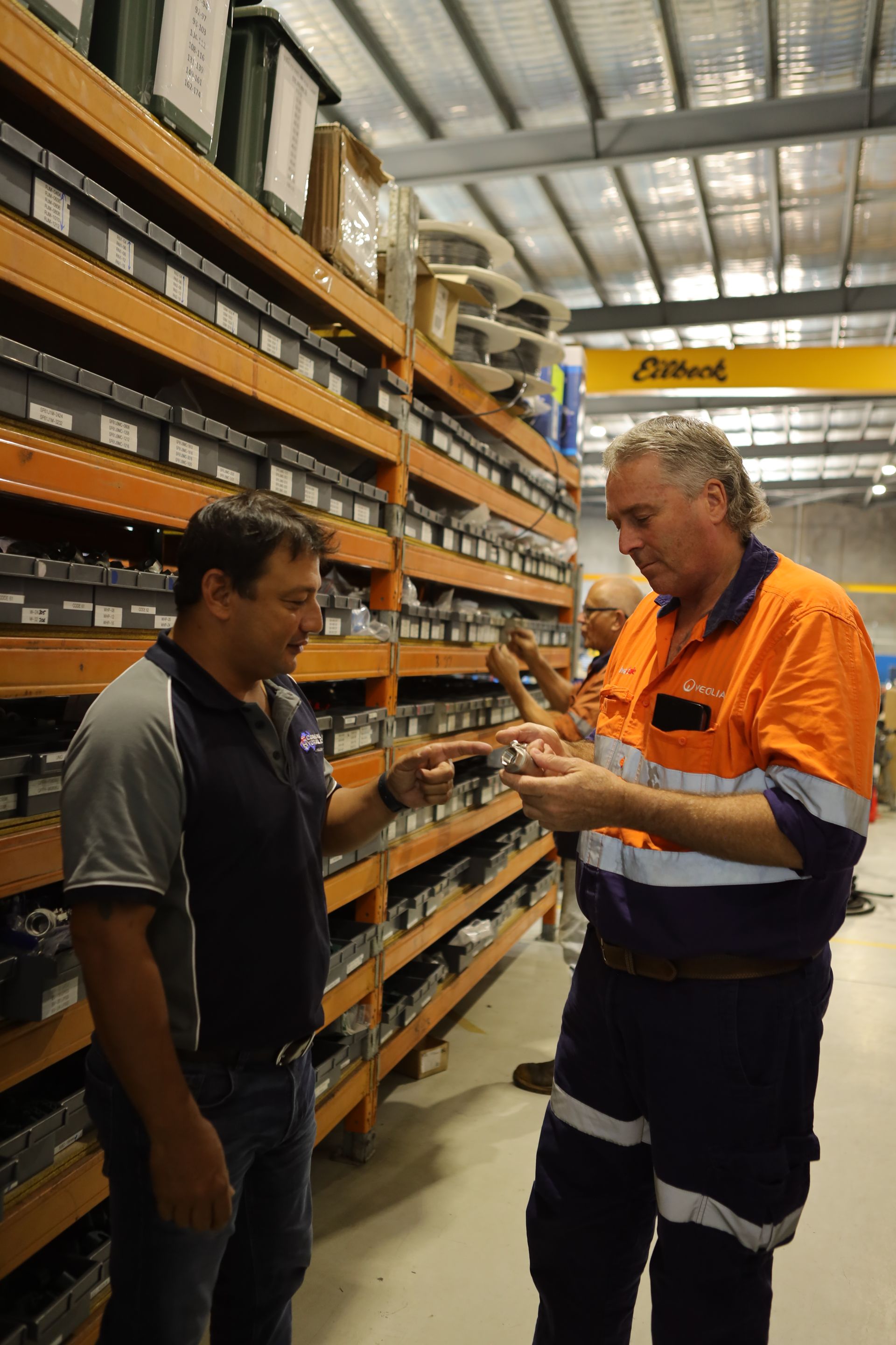 Two Men Are Standing In A Warehouse Talking To Each Other — Coastal Hydraulics & Engineering Pty Ltd In Bungalow, QLD