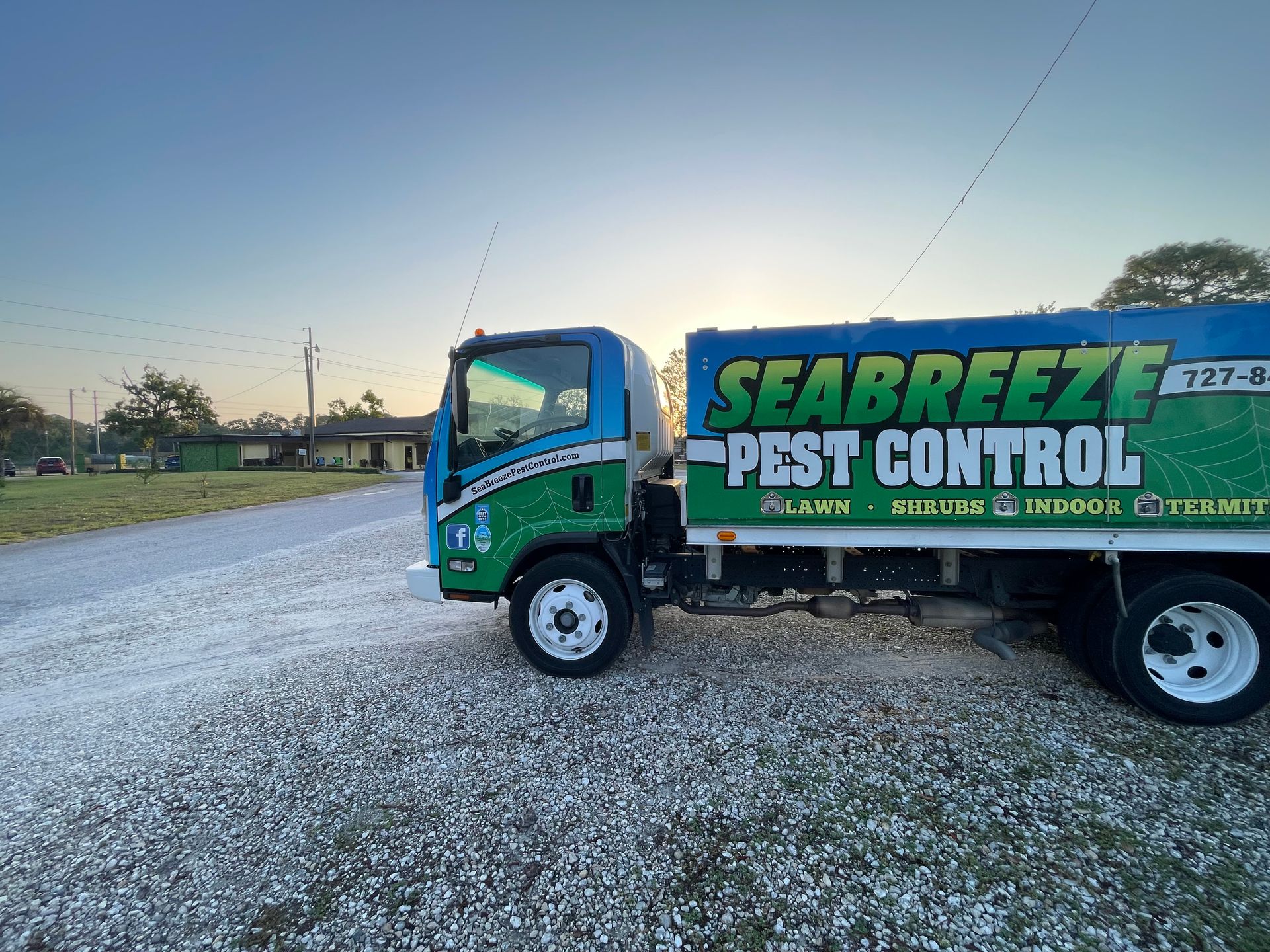 Seabreeze Pest Control truck parked on gravel road at sunrise. Green and blue truck, residential background.