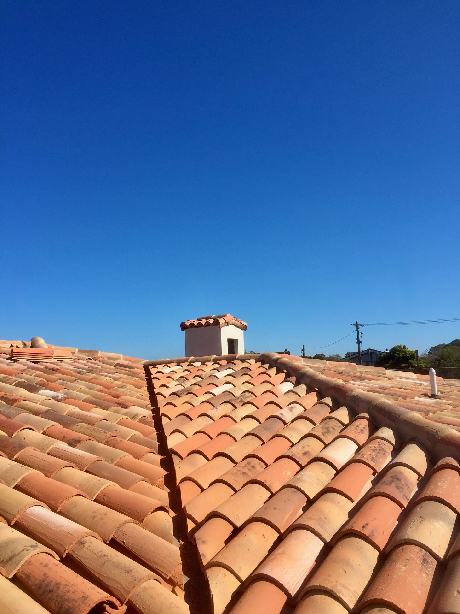 A terra-cotta tile roof under a clear blue sky with a small chimney visible at the peak.