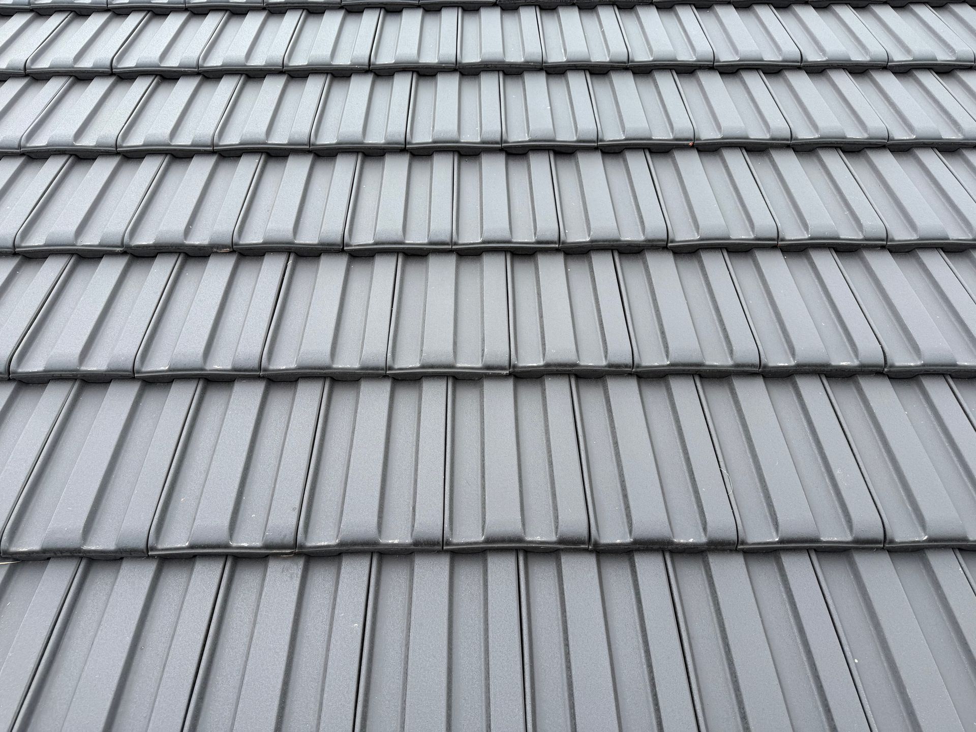 A close-up of a gray, tiled roof with repeating, uniform vertical patterns.