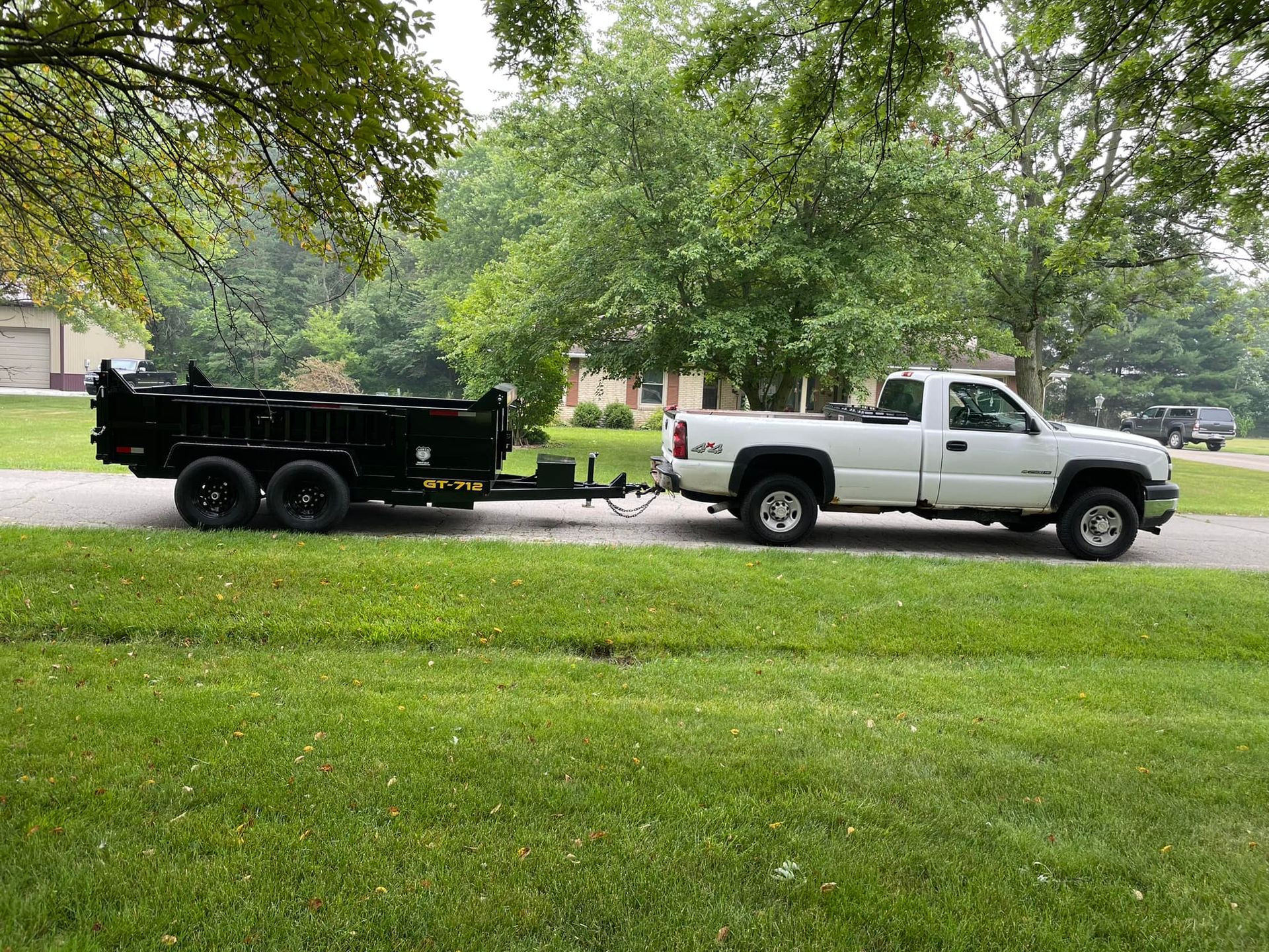 A white truck is towing a black dump trailer.
