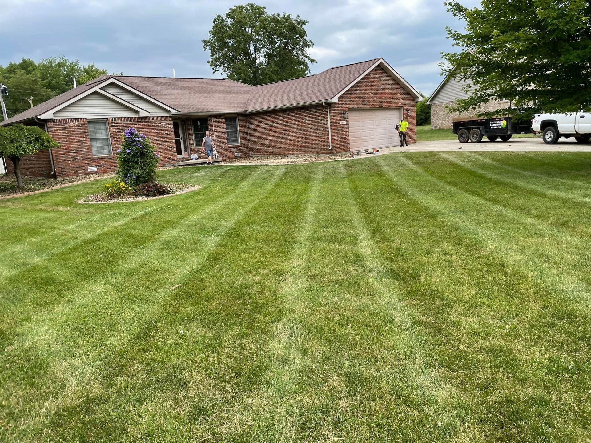 A lush green lawn in front of a brick house with a truck parked in the driveway.