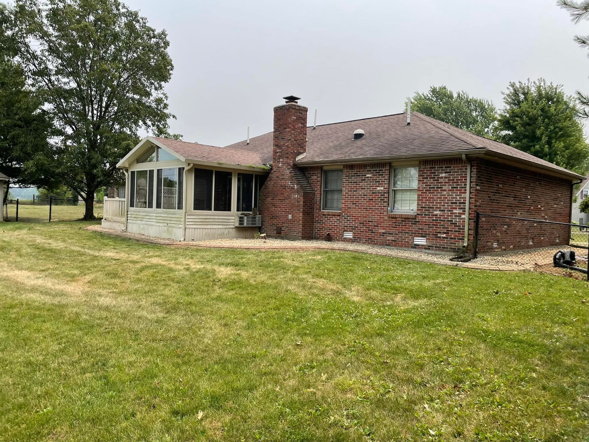 A brick house with a screened in porch and a large lawn in front of it.