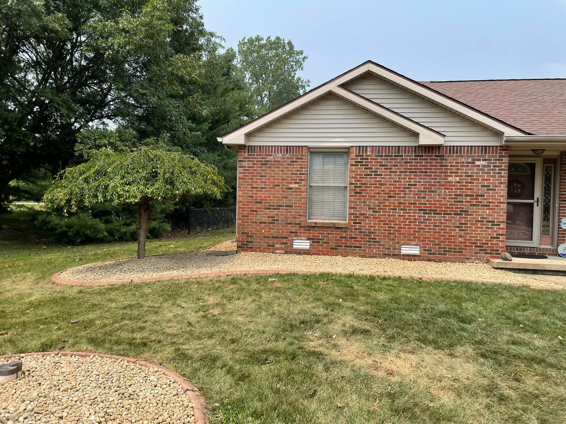 A brick house with a white siding and a tree in front of it.