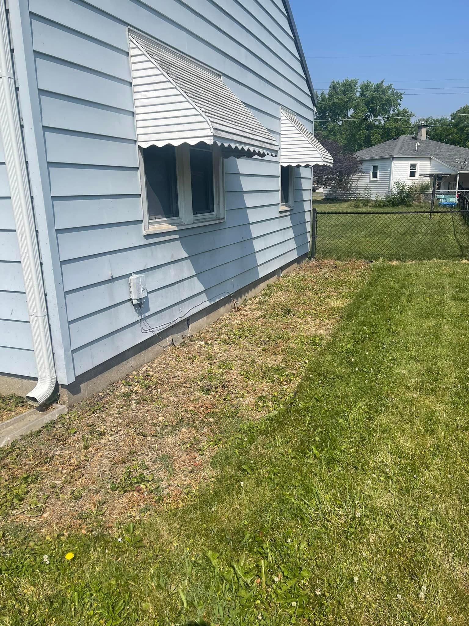 A house with a white awning on the windows and a lawn in front of it.
