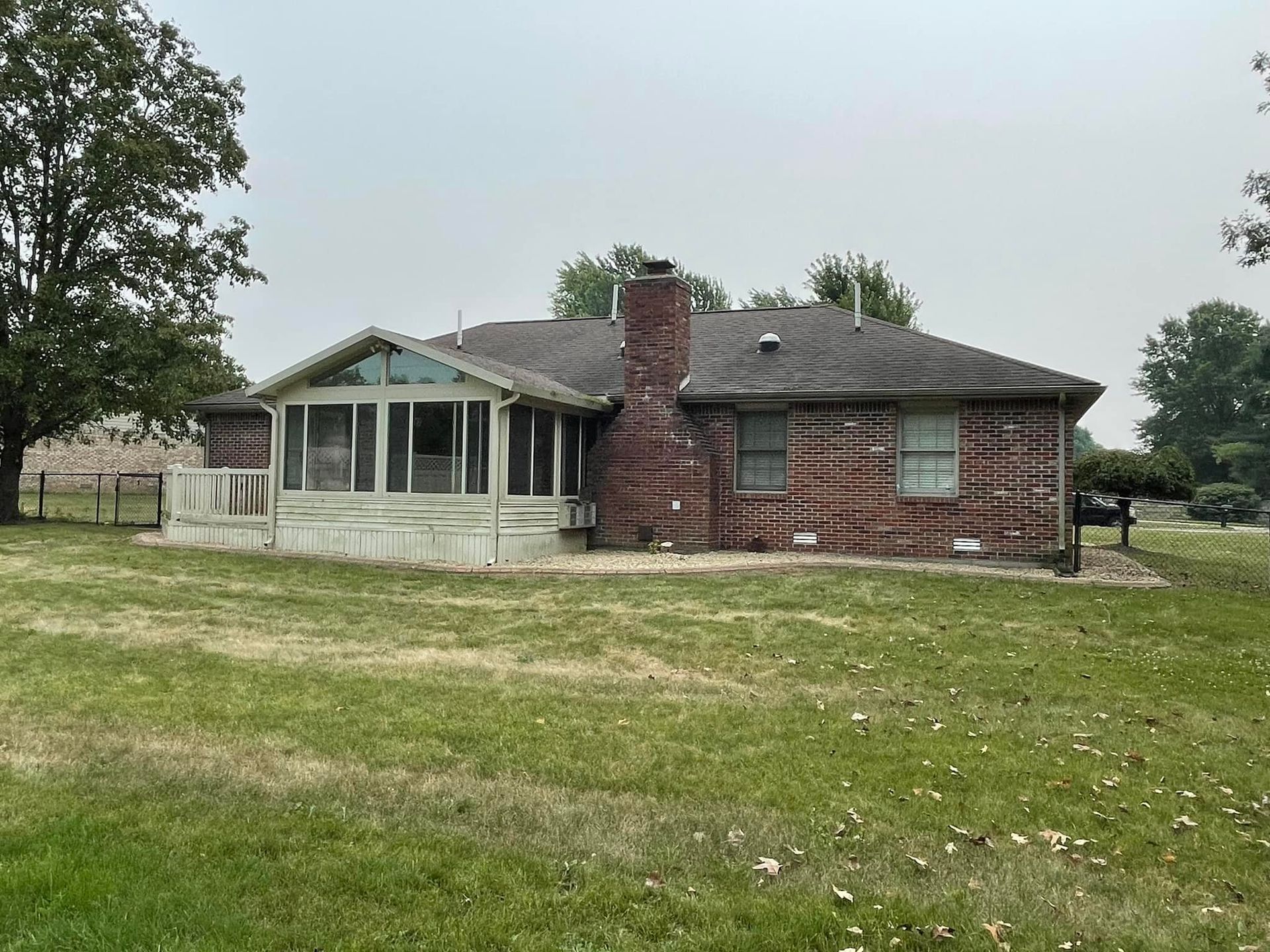 A brick house with a screened in porch and a large lawn in front of it.