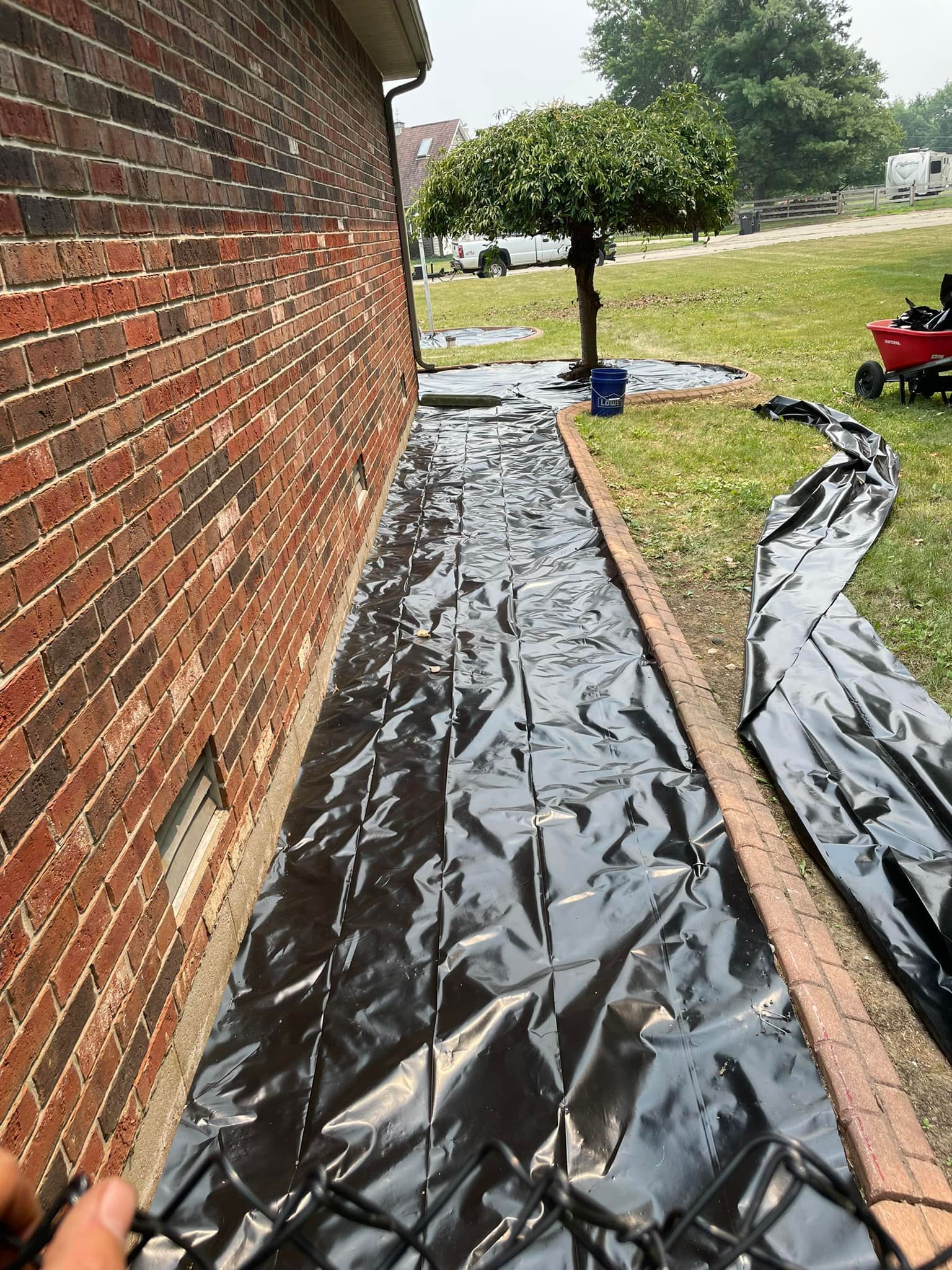 A person is holding a chain link fence in front of a brick wall.