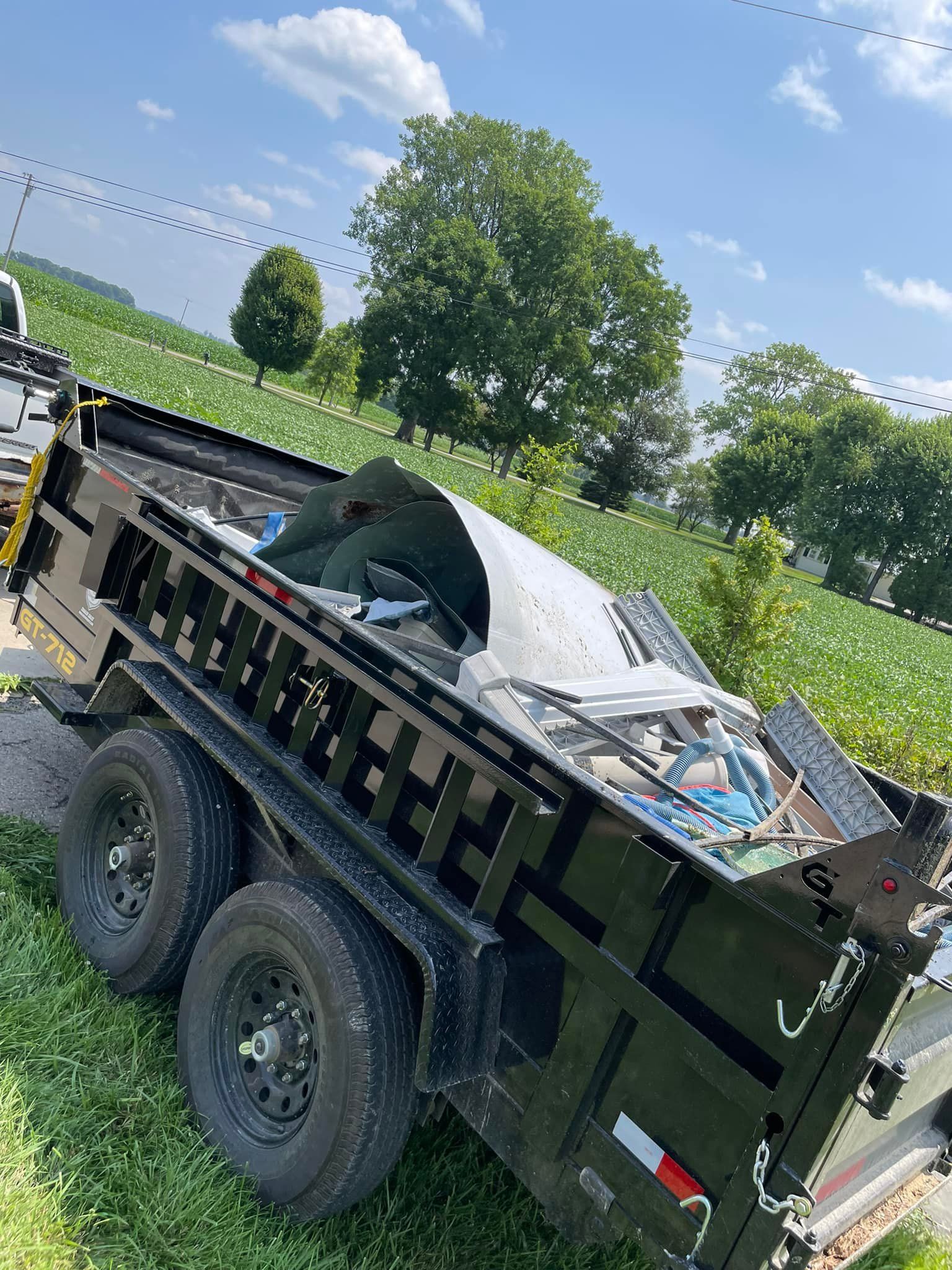 A dumpster is sitting in the grass next to a truck.