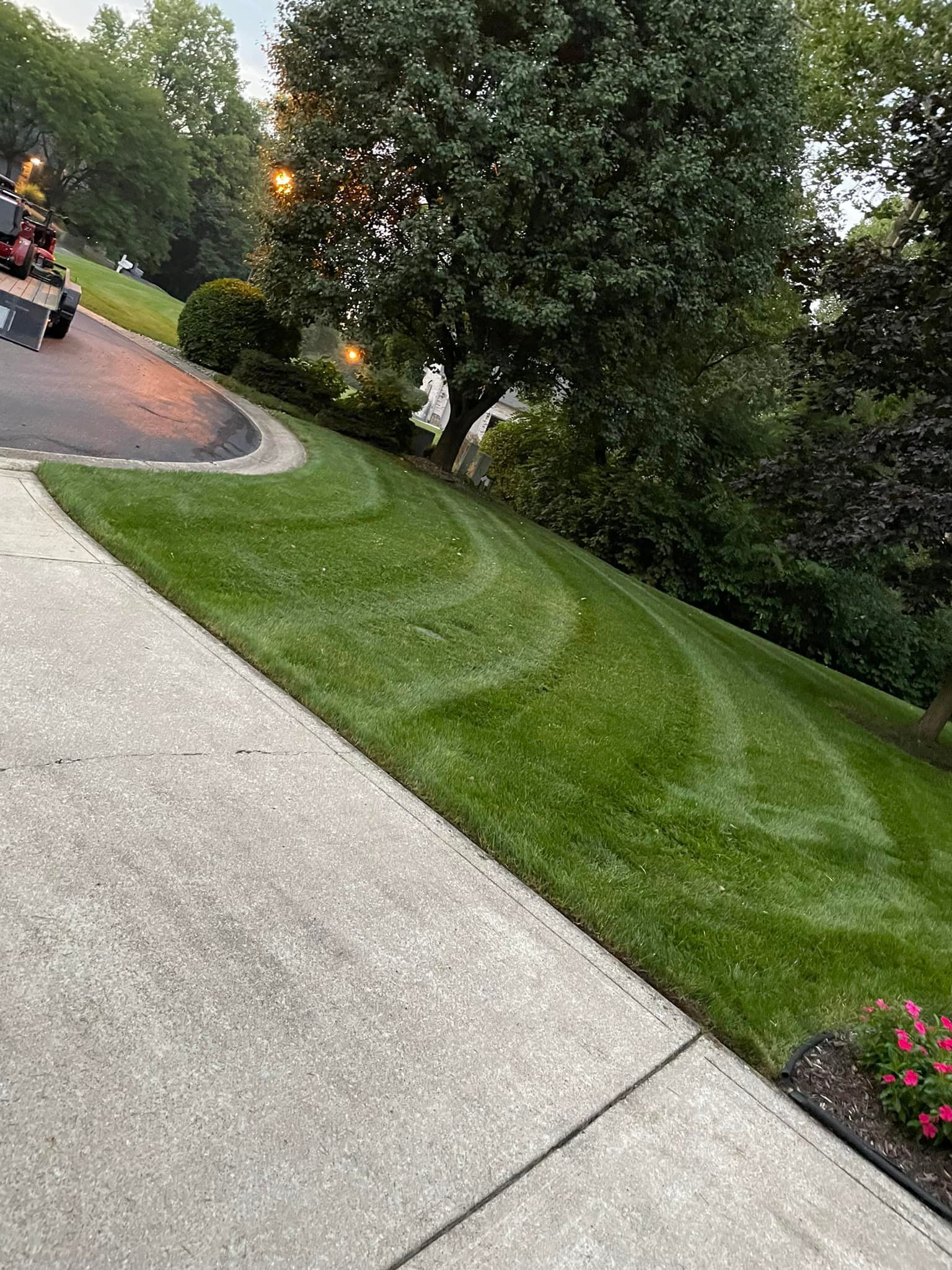 A lawn mower is cutting a lush green lawn next to a sidewalk.