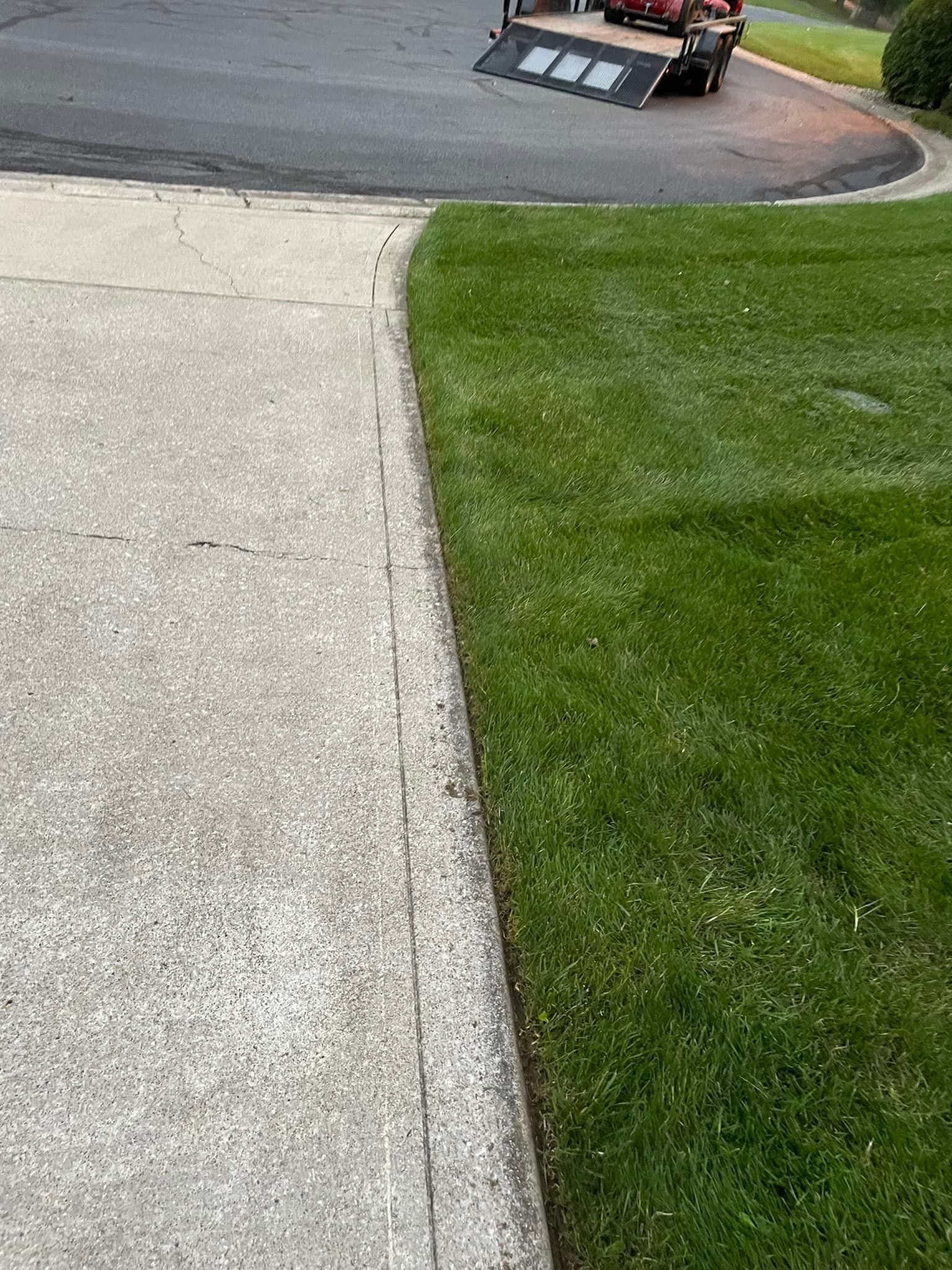 A lawn mower is cutting the grass next to a concrete driveway.
