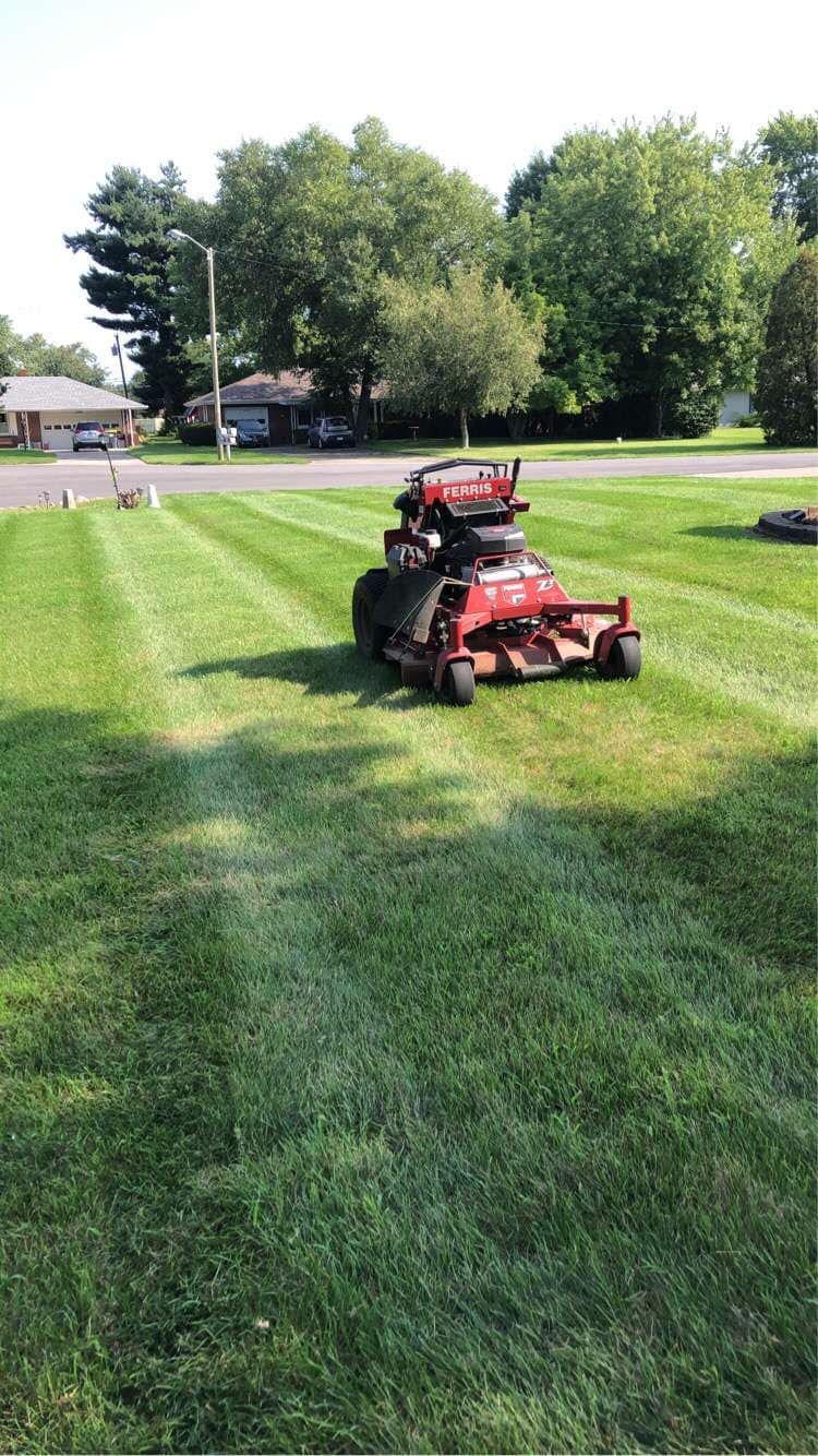 A red lawn mower is cutting a lush green lawn.