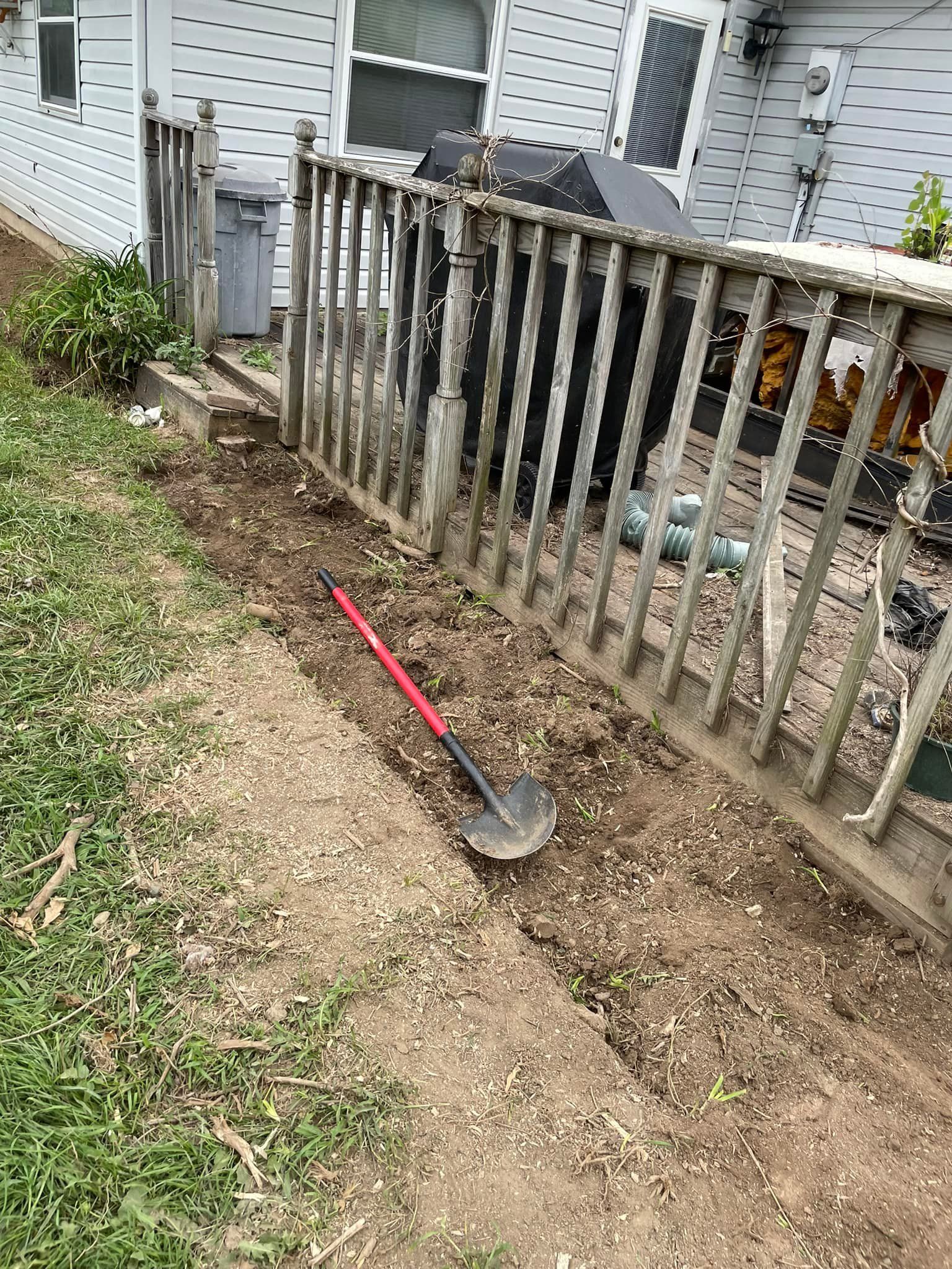 A shovel is sitting in the dirt next to a wooden fence.