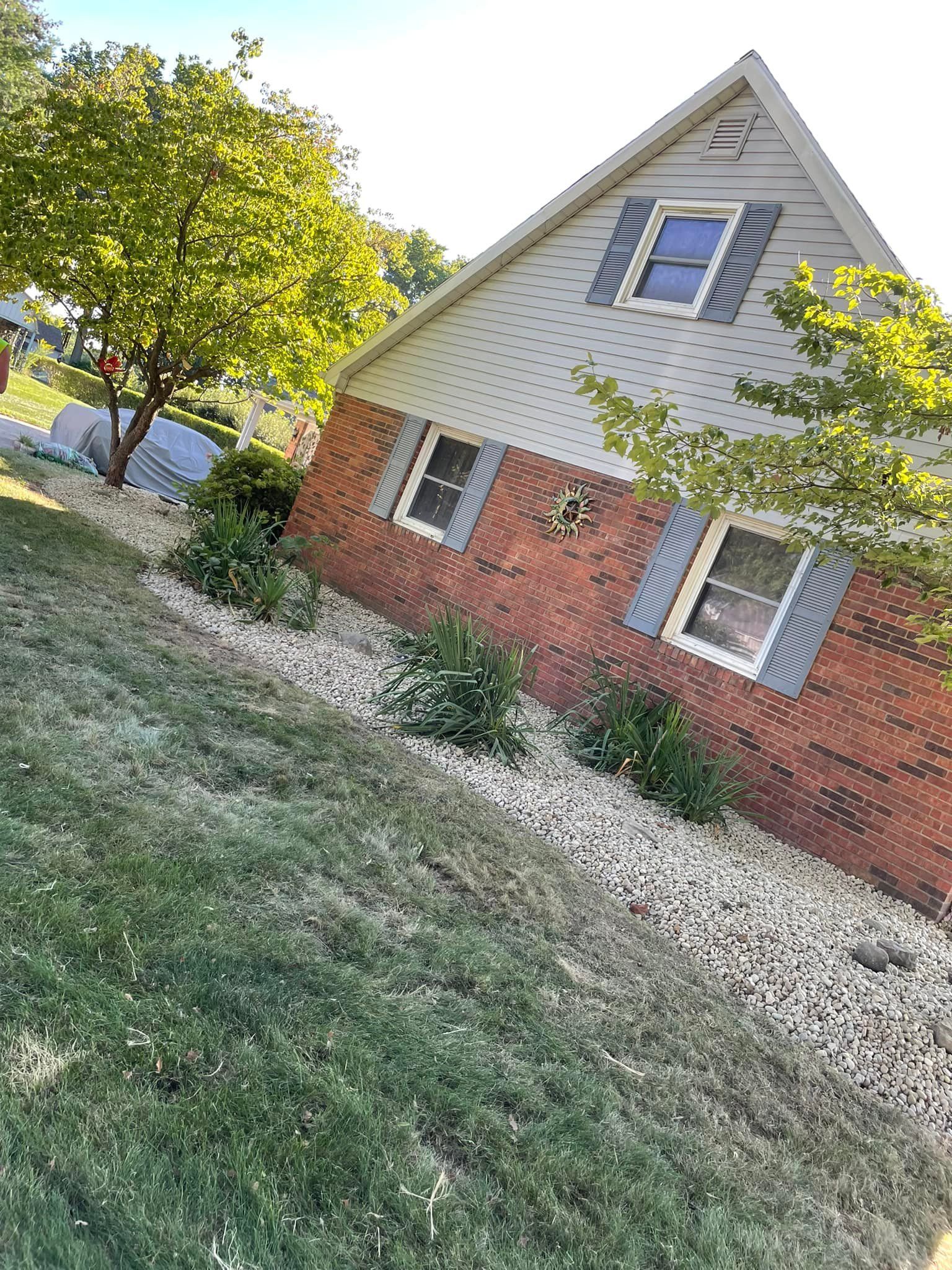 A brick house with a white siding and blue shutters is sitting on top of a lush green lawn.