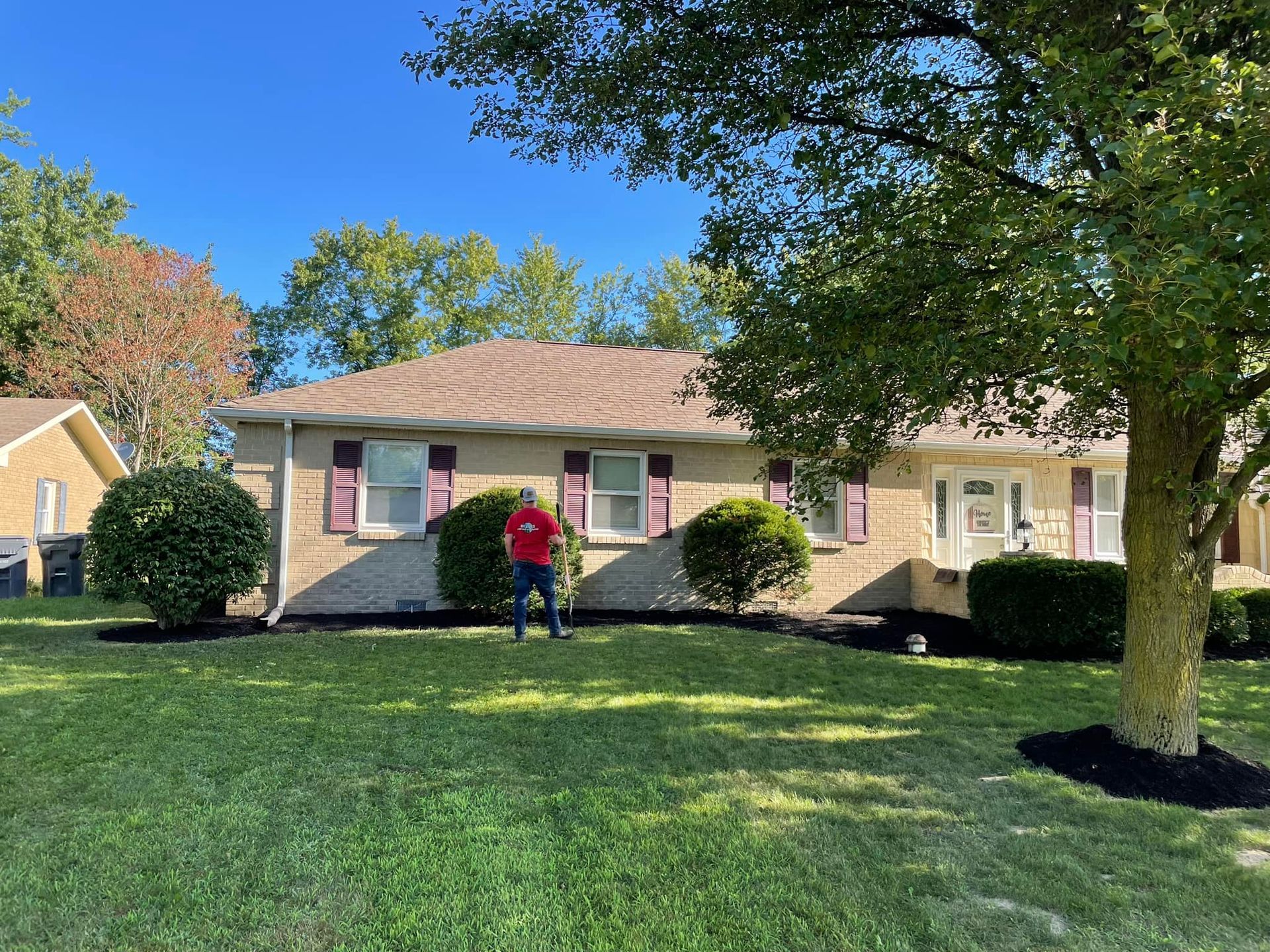 A man in a red shirt is standing in front of a house.