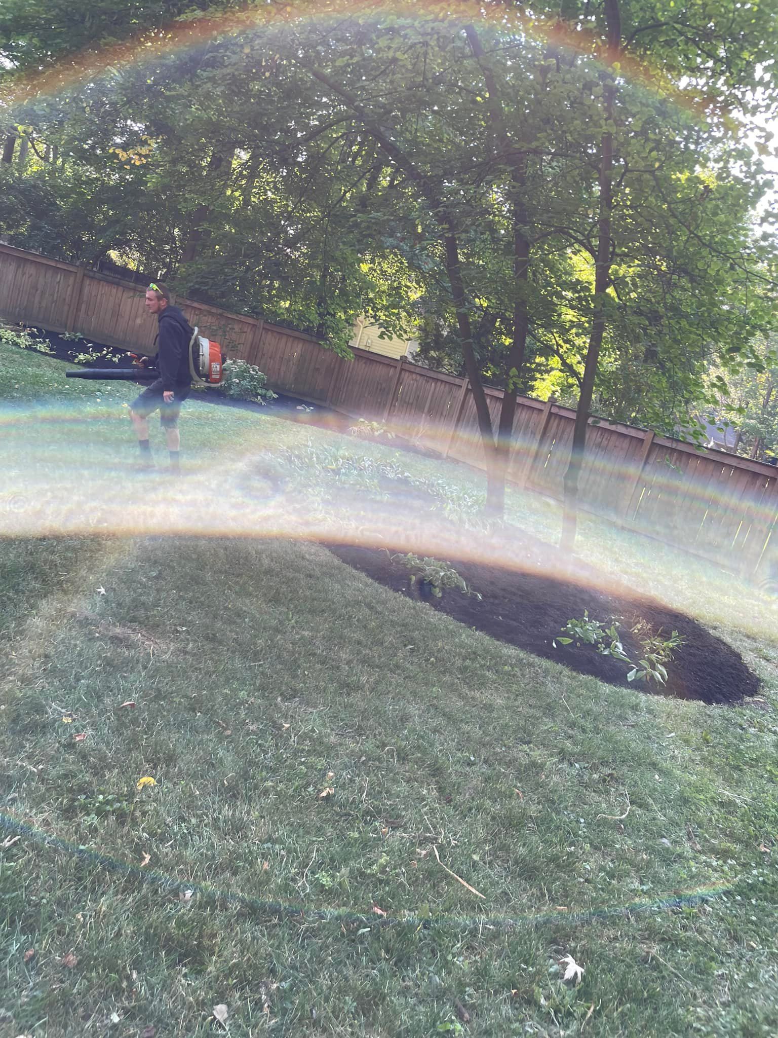 A person is walking in the grass with a rainbow in the background.