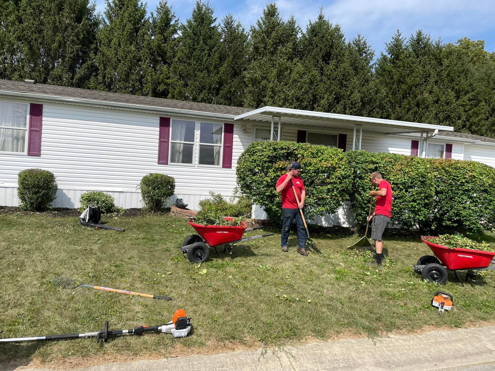 Two men are raking the grass in front of a mobile home.
