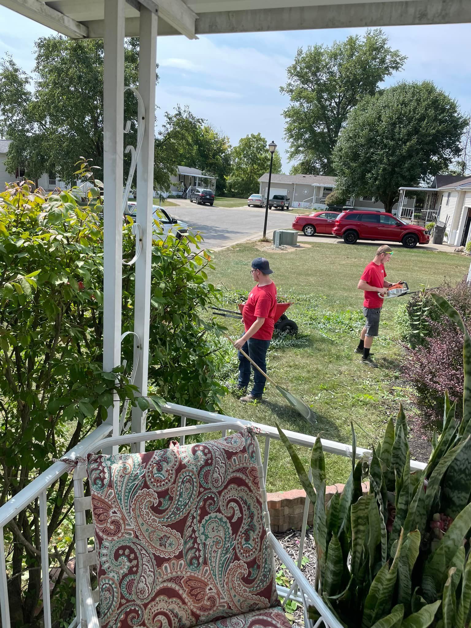Two men are mowing the grass on the porch of a house.