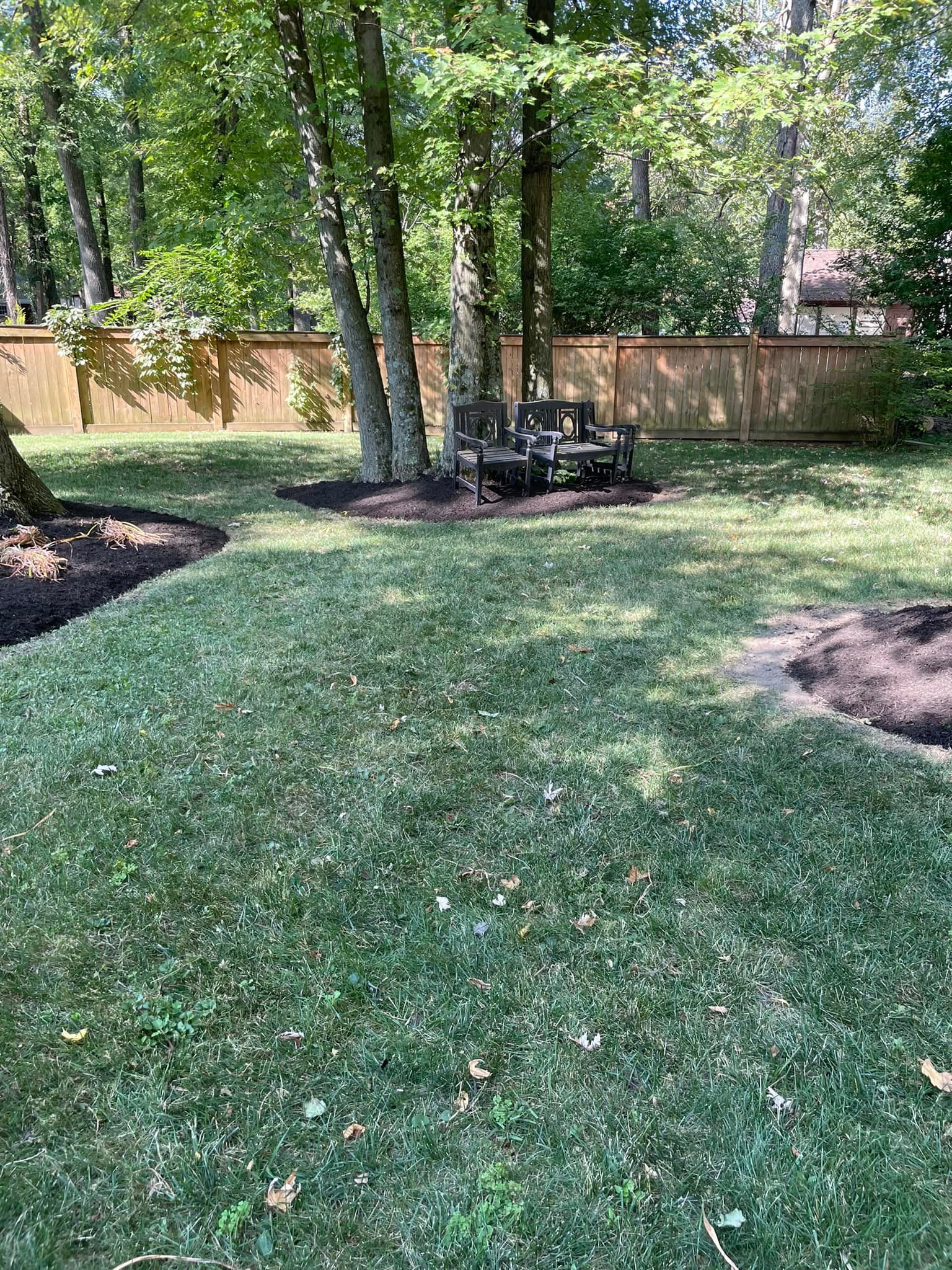 A lush green lawn with a wooden fence and trees in the background.