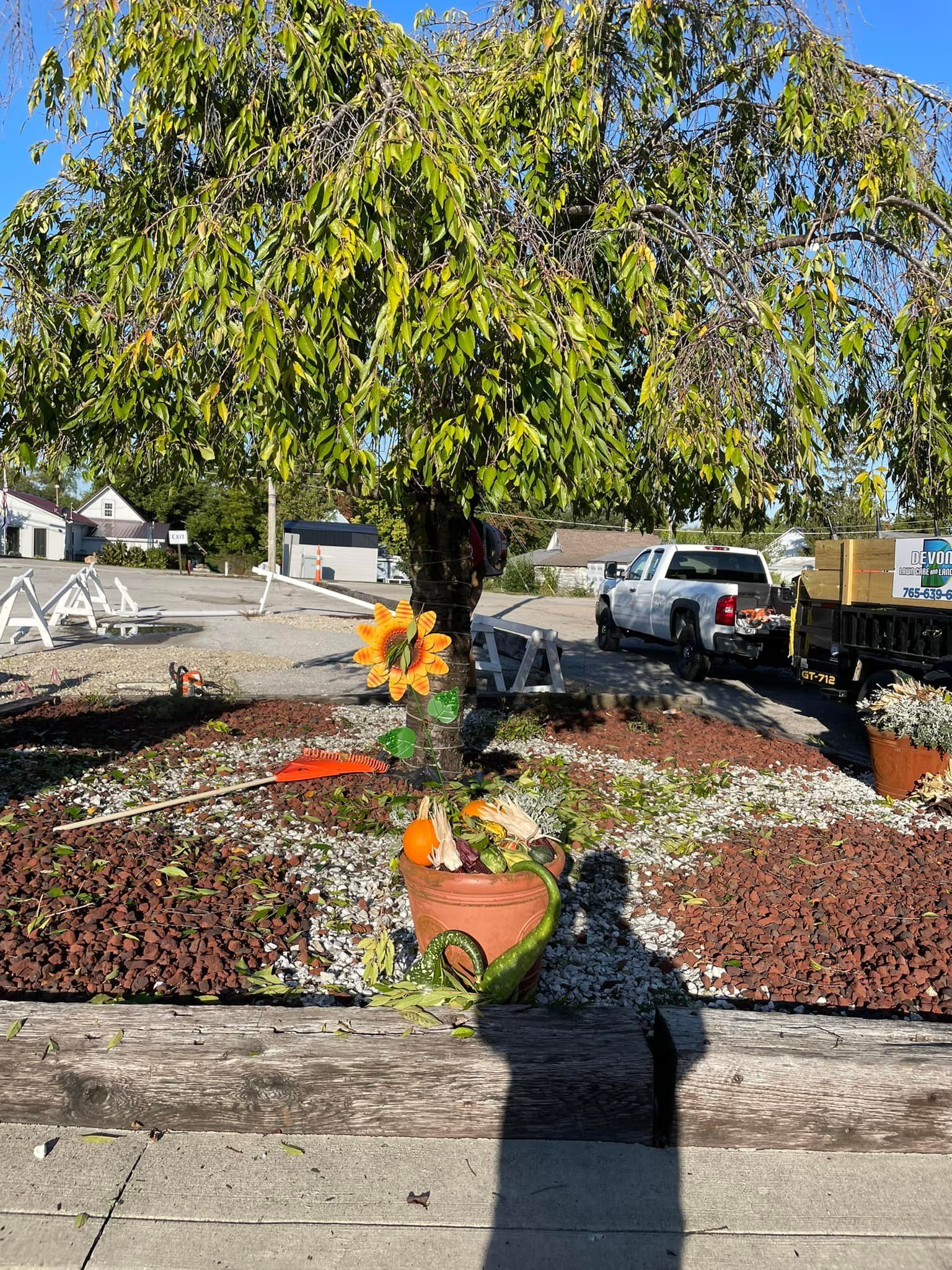 A white truck is parked in front of a tree with a sunflower in a pot.