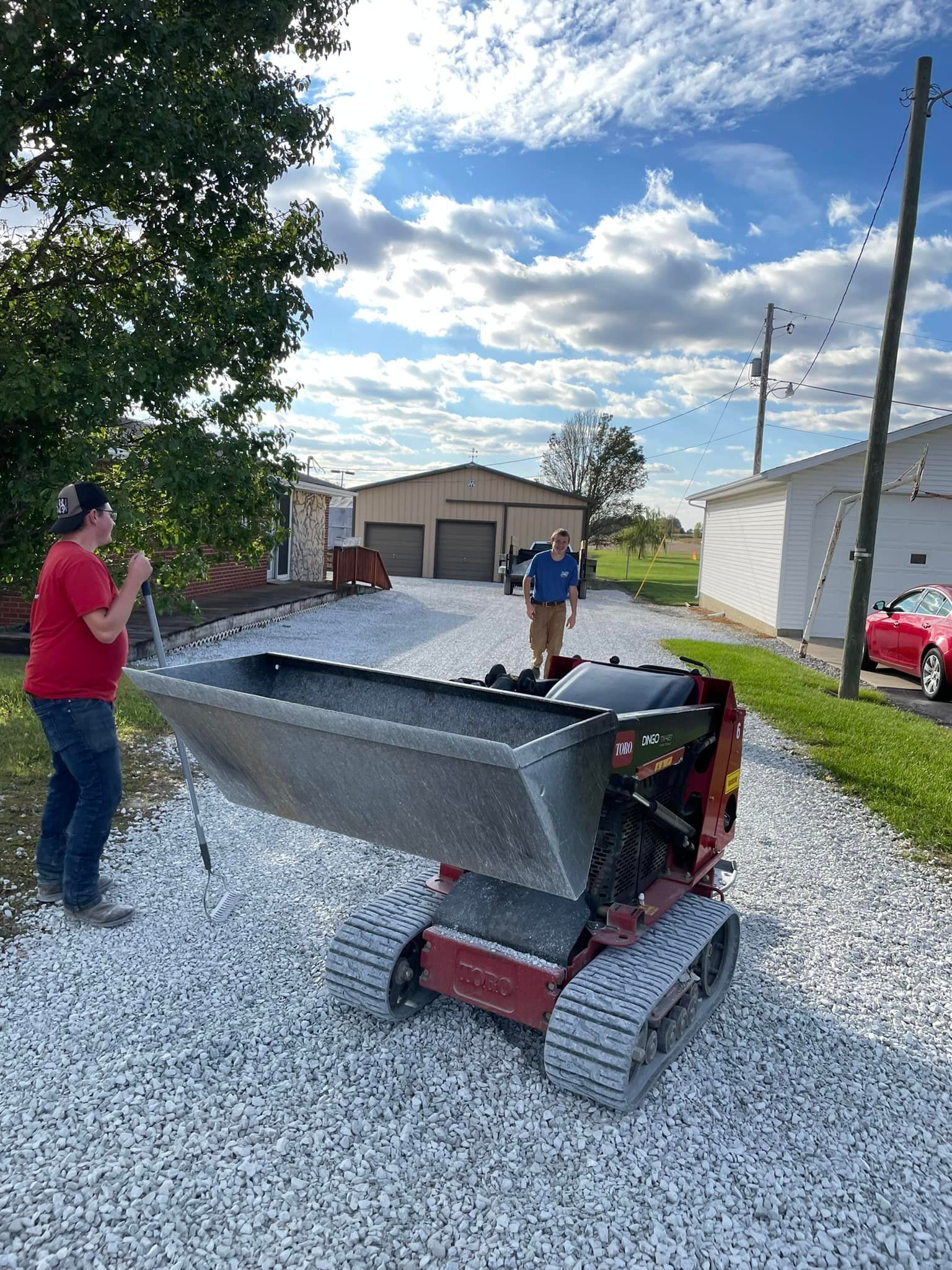 A man is standing next to a dump truck on a gravel road.