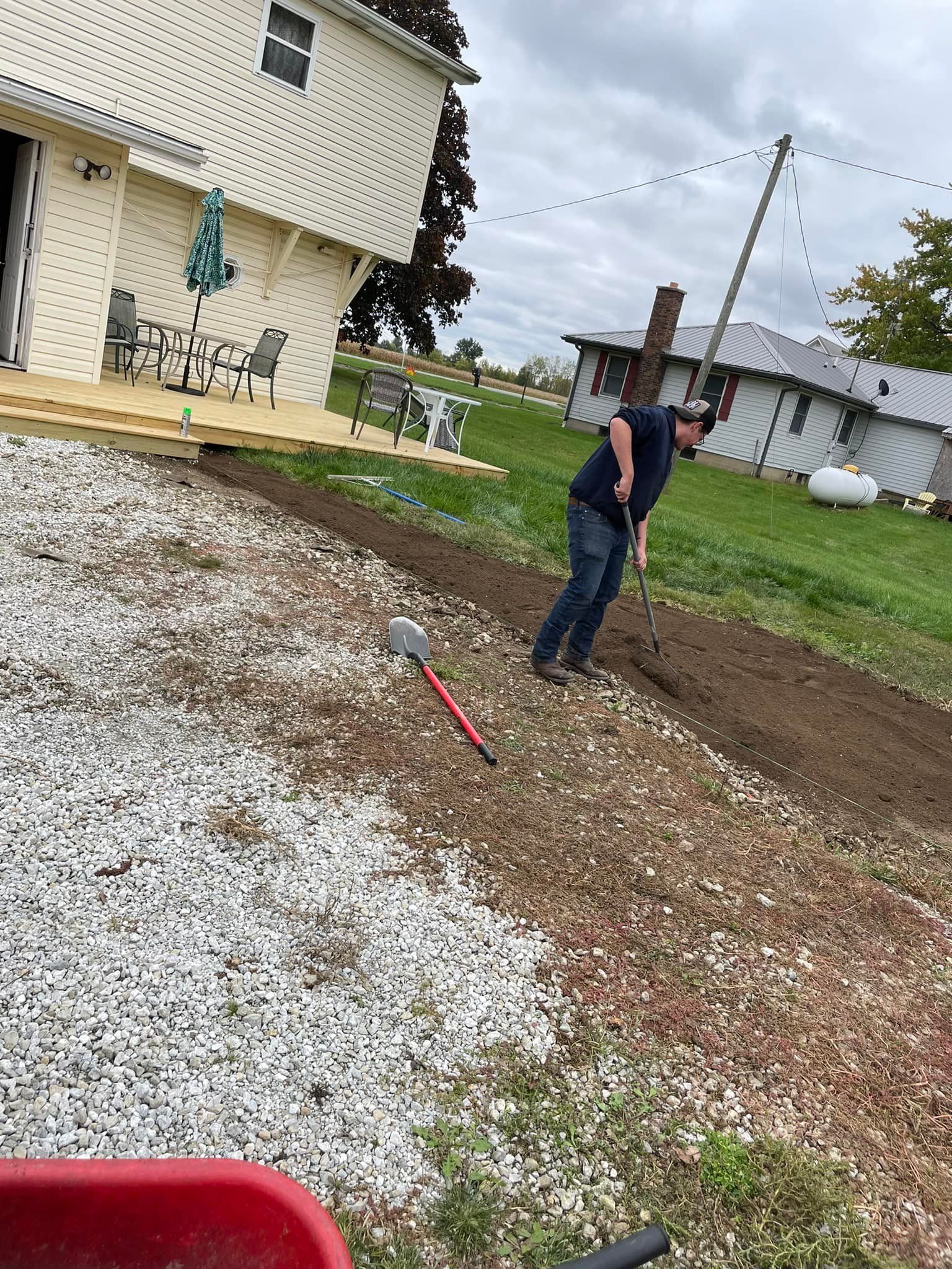 A man is raking dirt in front of a house.