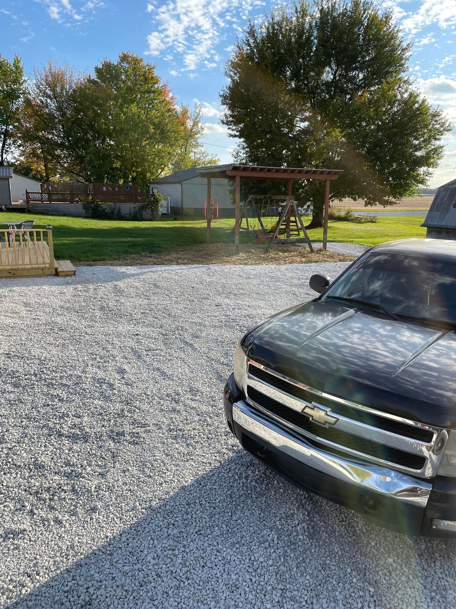 A black truck is parked in a gravel lot in front of a house.