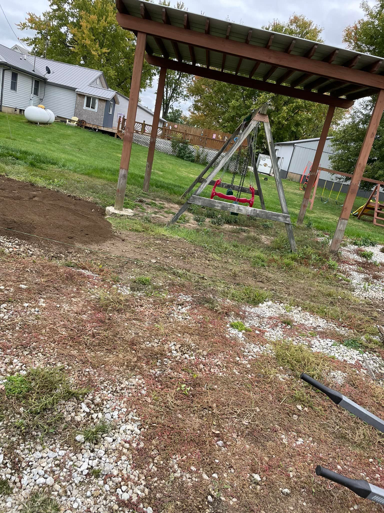 A swing set is sitting under a wooden pergola in a yard.