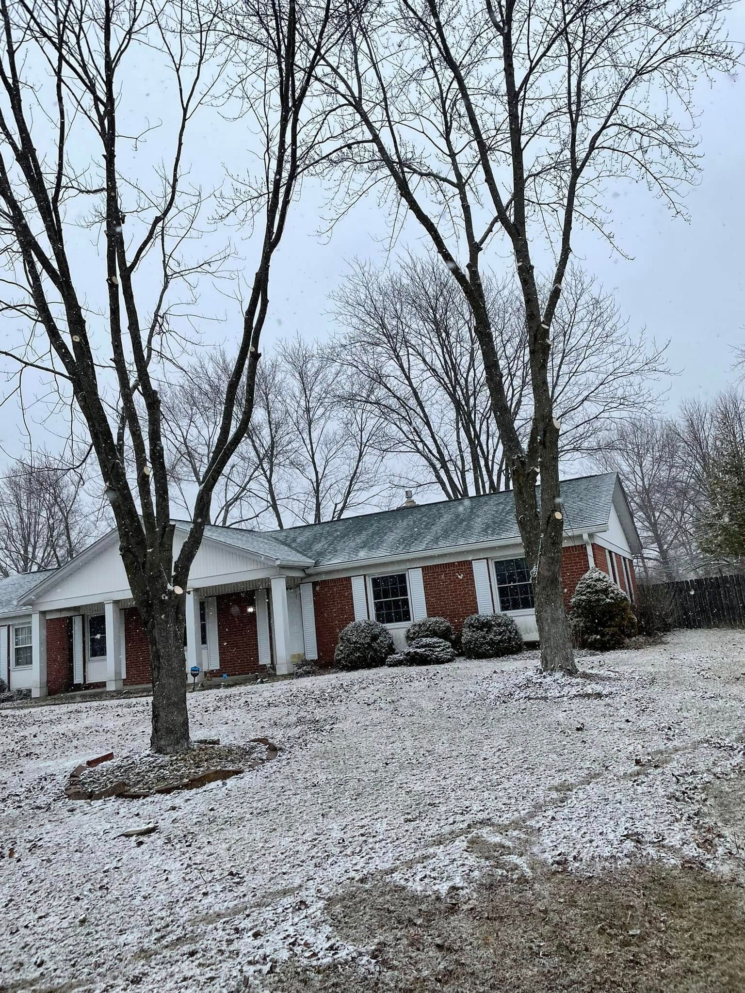 A house with a lot of snow on the ground and trees in front of it.