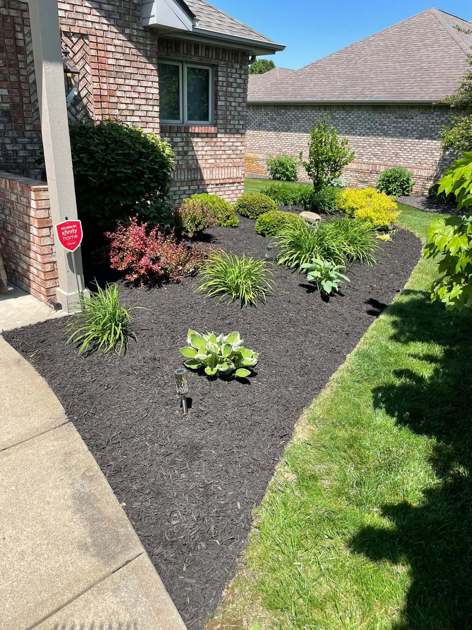 A yard with a lot of plants and mulch in front of a house.
