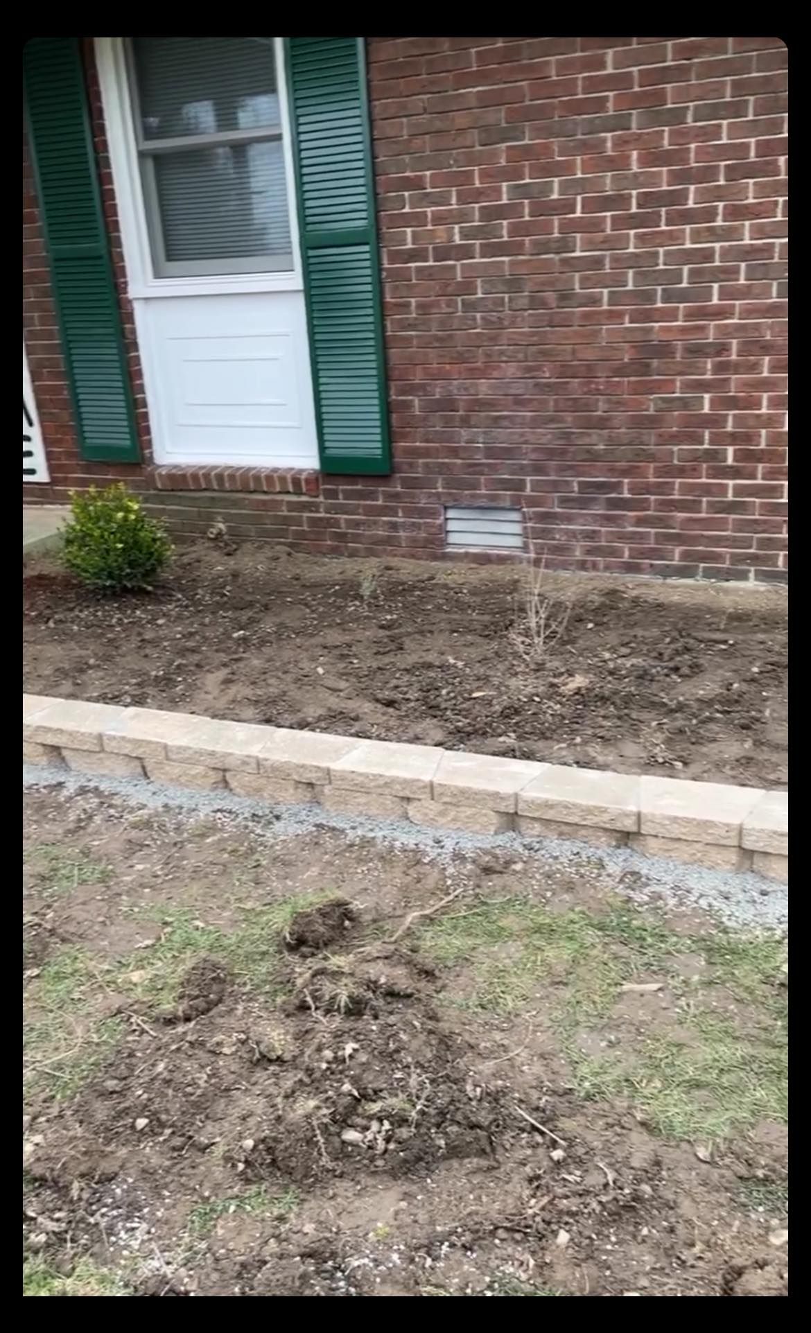 A brick house with a white door and green shutters is being remodeled.