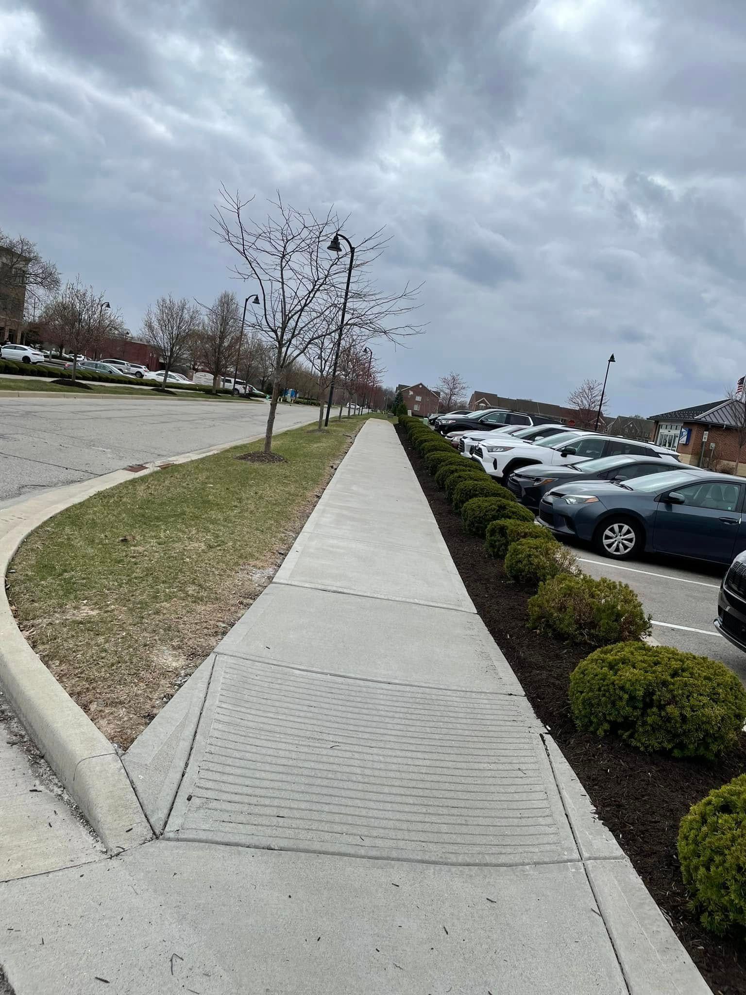 A sidewalk leading to a parking lot with cars parked on the side of it.