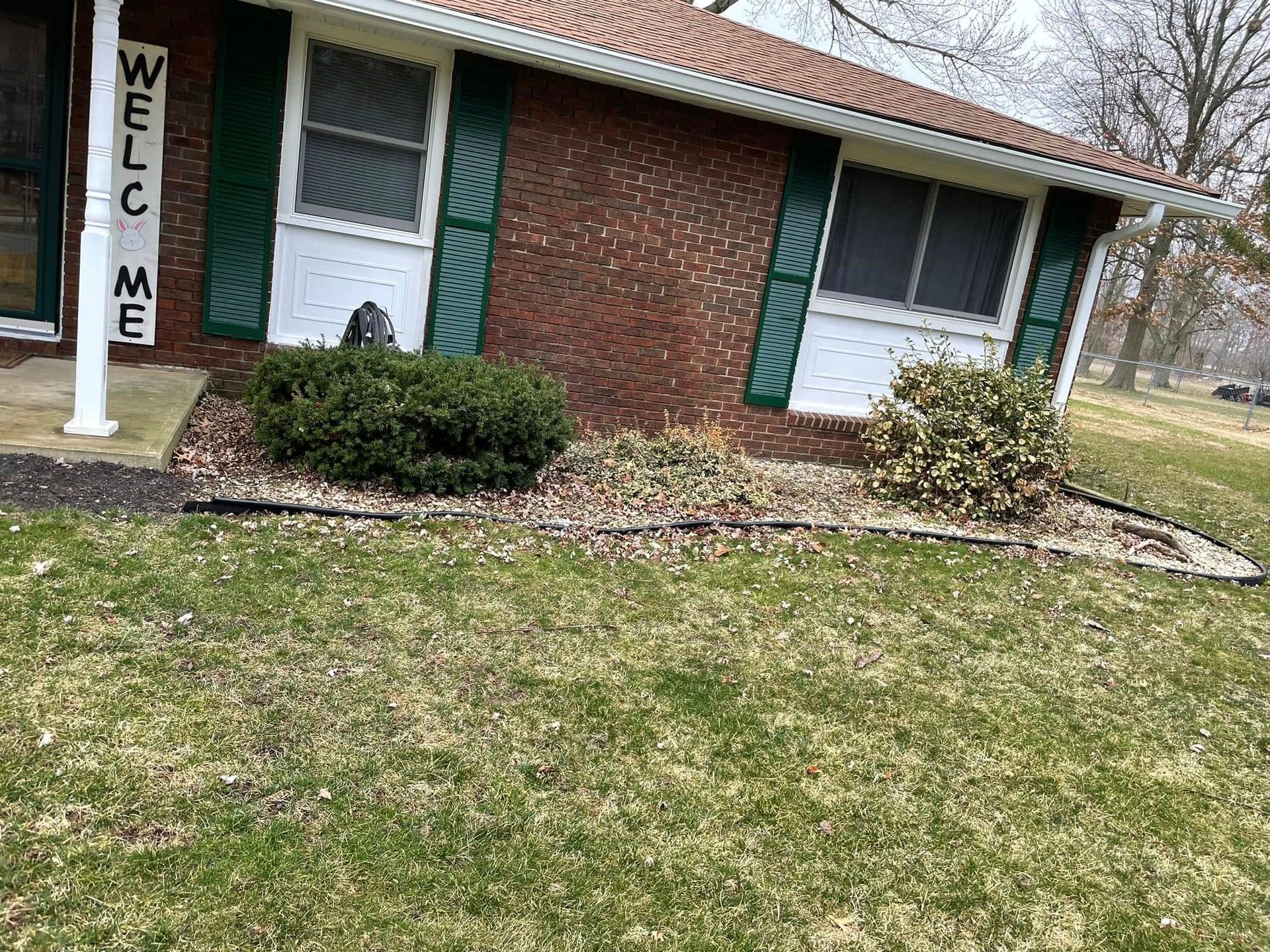 A brick house with green shutters and a welcome sign in front of it.