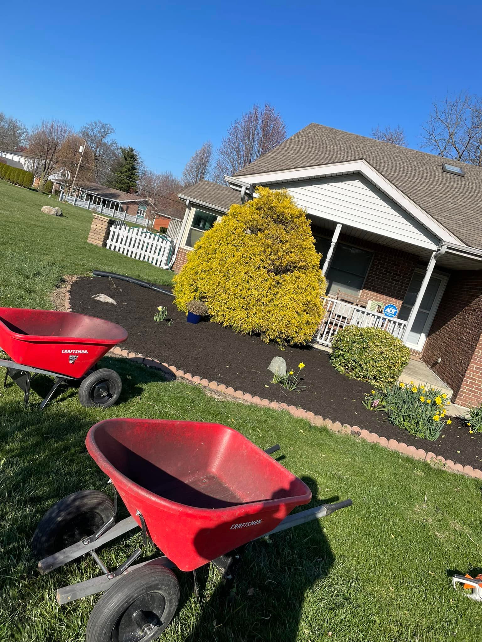 Two red wheelbarrows are parked in front of a house.