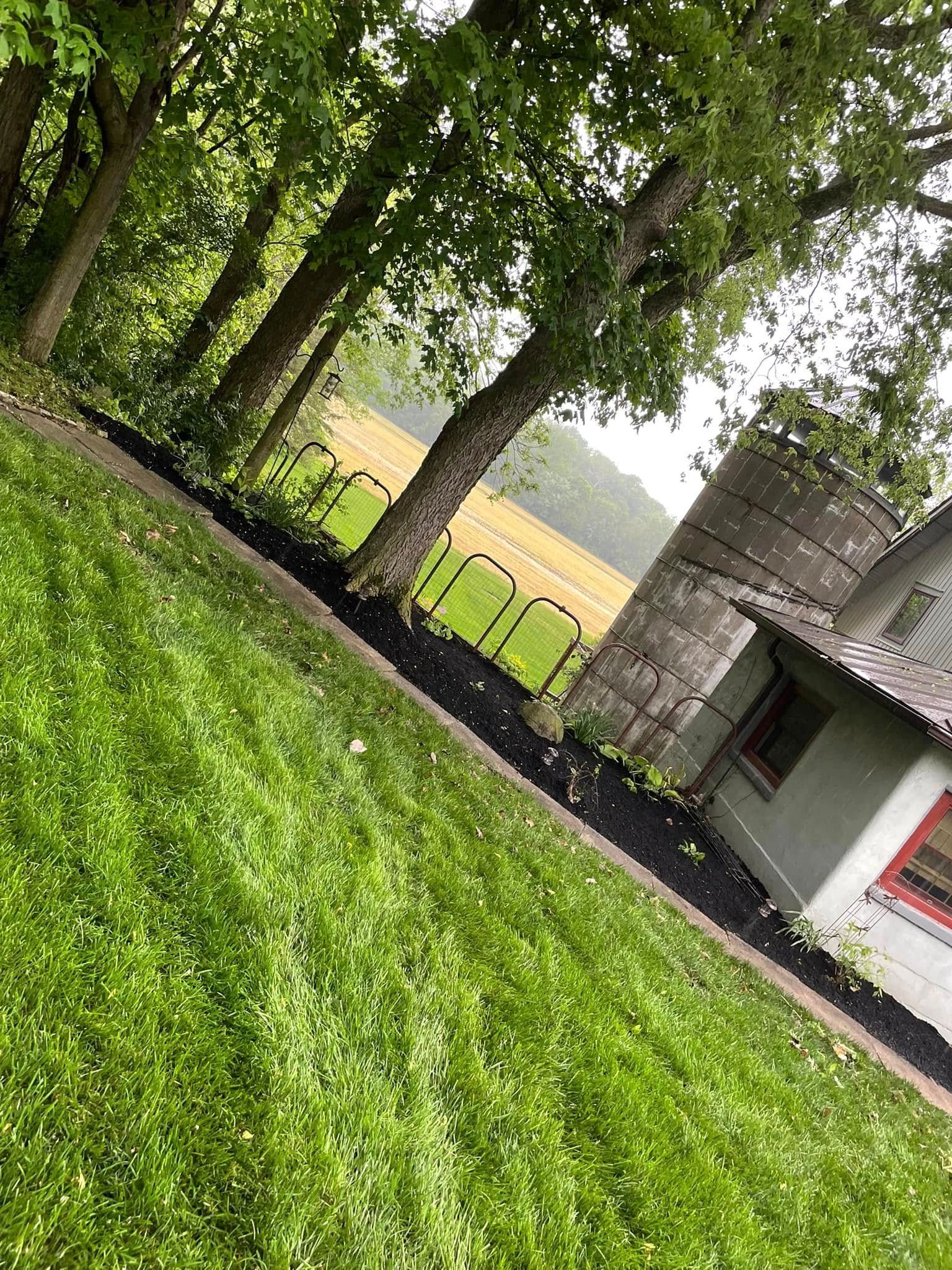 A house with a silo in the background is surrounded by trees and grass.