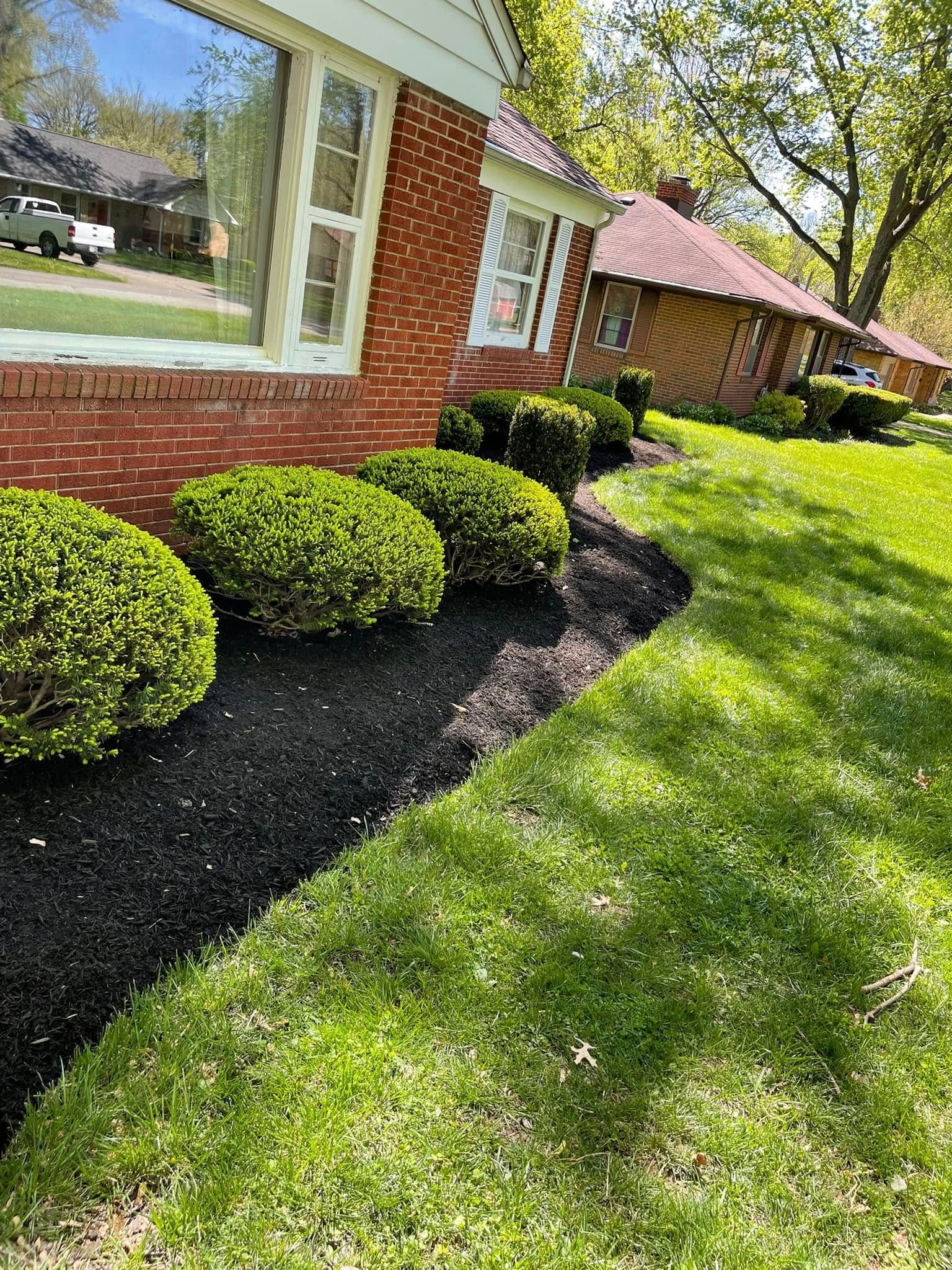A brick house with a lush green lawn and bushes in front of it.