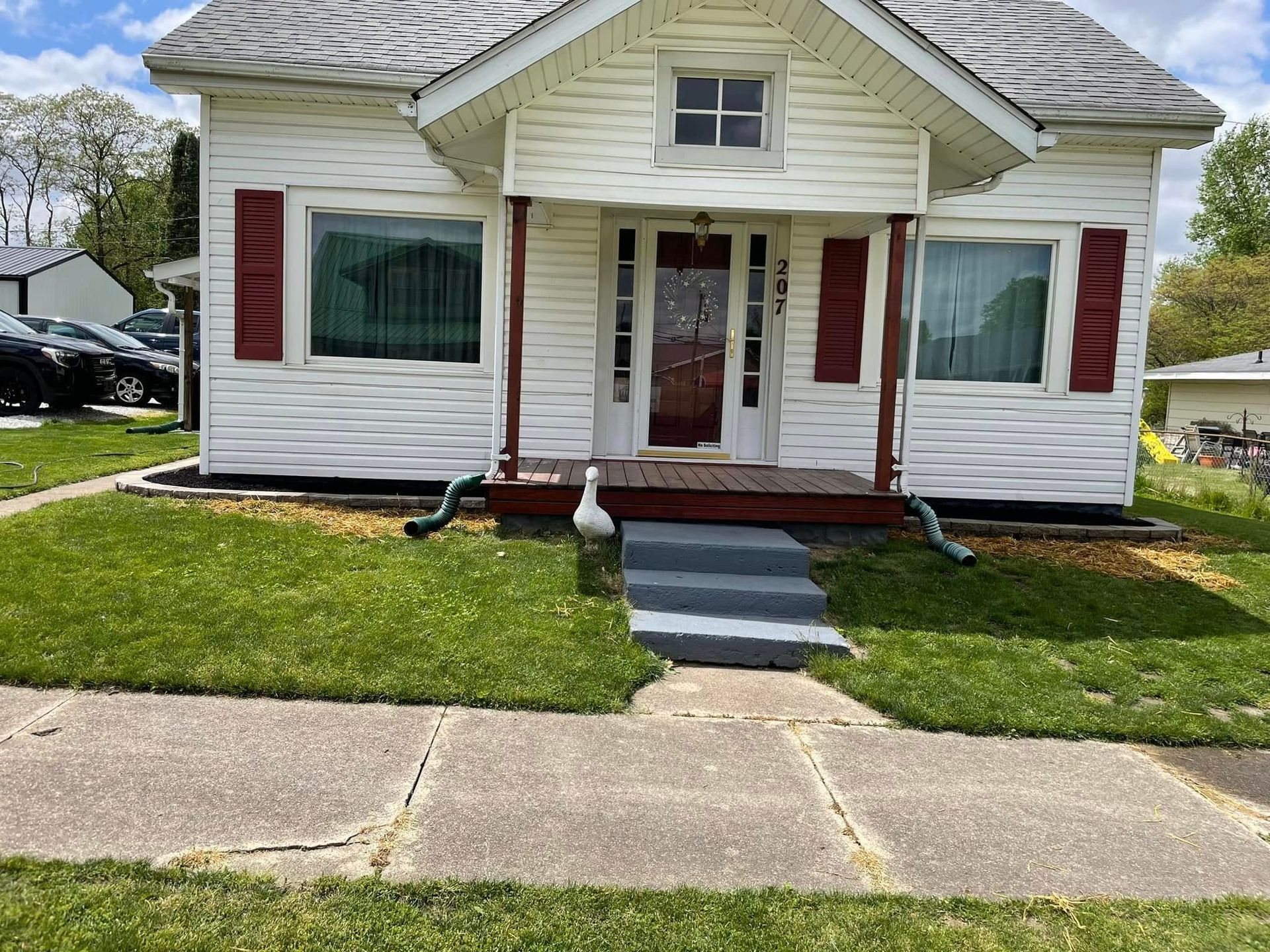 A small white house with red shutters is sitting on top of a lush green lawn.