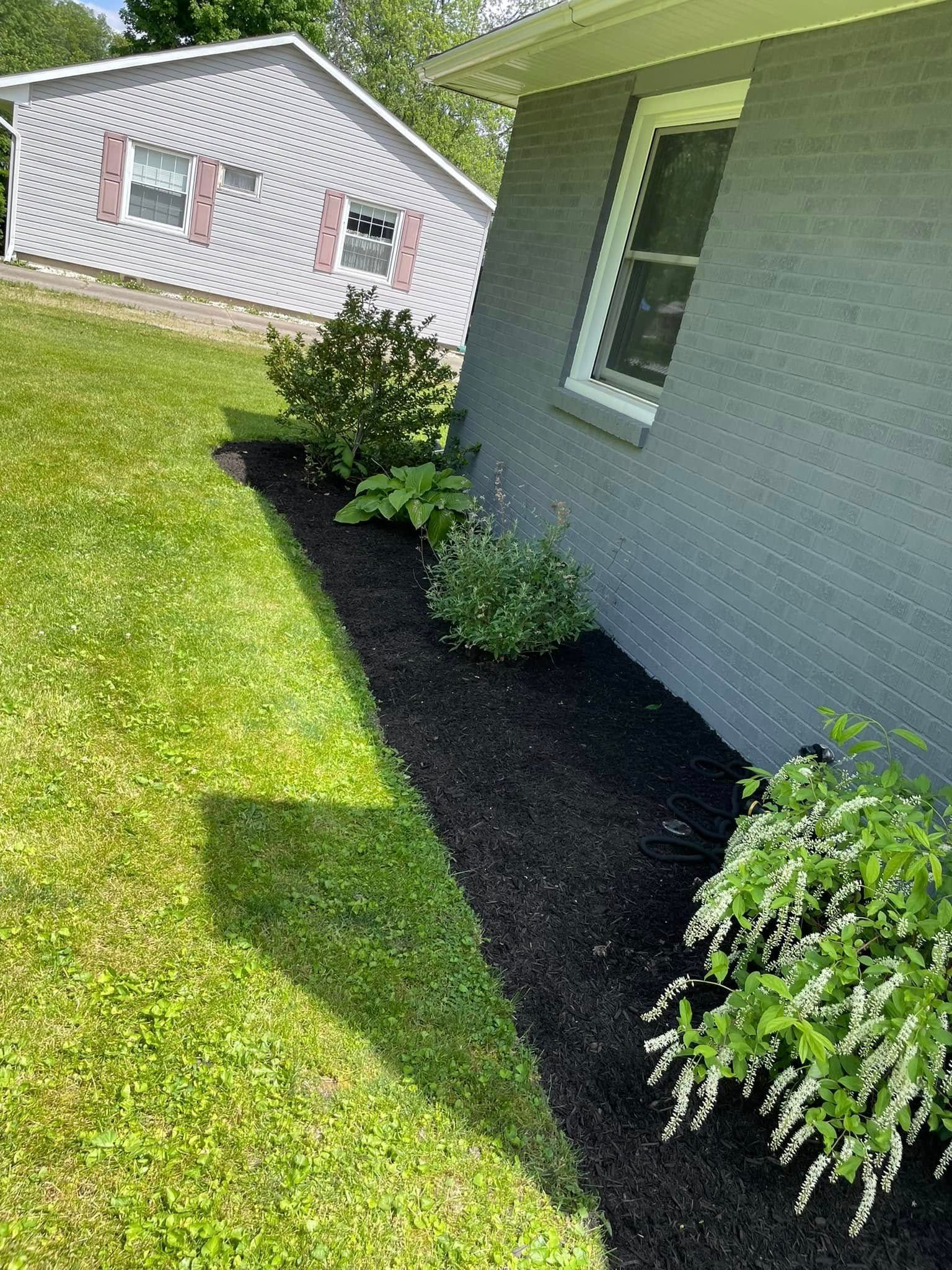 A house with a lush green lawn and a black mulch bed in front of it.
